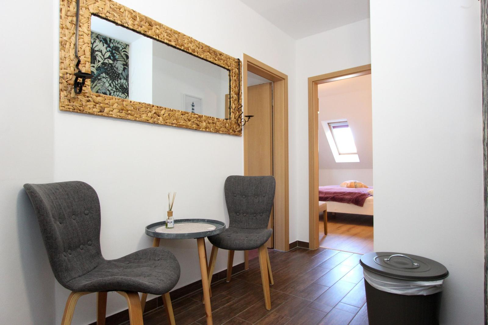 Eingangsbereich mit zwei Stühlen und Tisch. Im Hintergrund ist ein Schlafzimmer mit Dachfenster sichtbar.