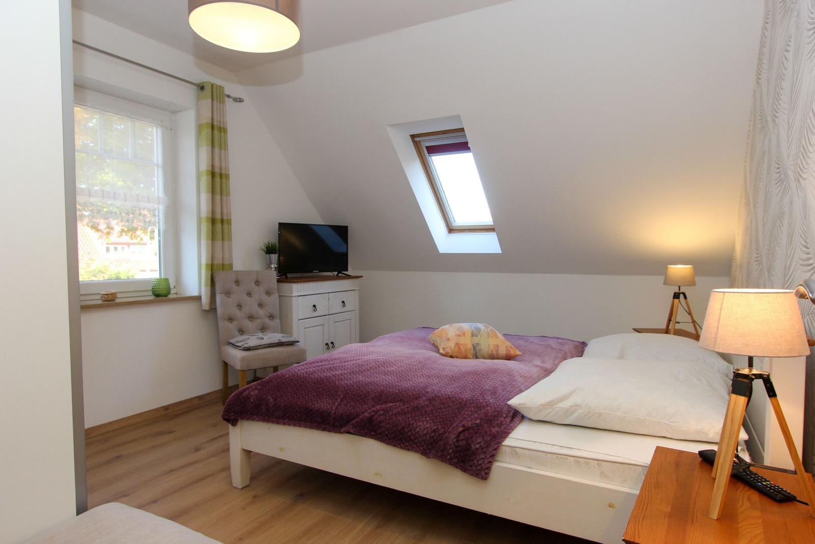 Schlafzimmer mit Dachschräge, Bett, TV und Fenster.