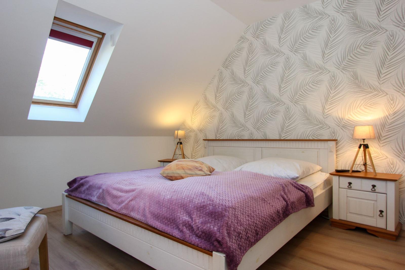 Schlafzimmer mit Dachfenster, Bett mit Laken und Nachttische.