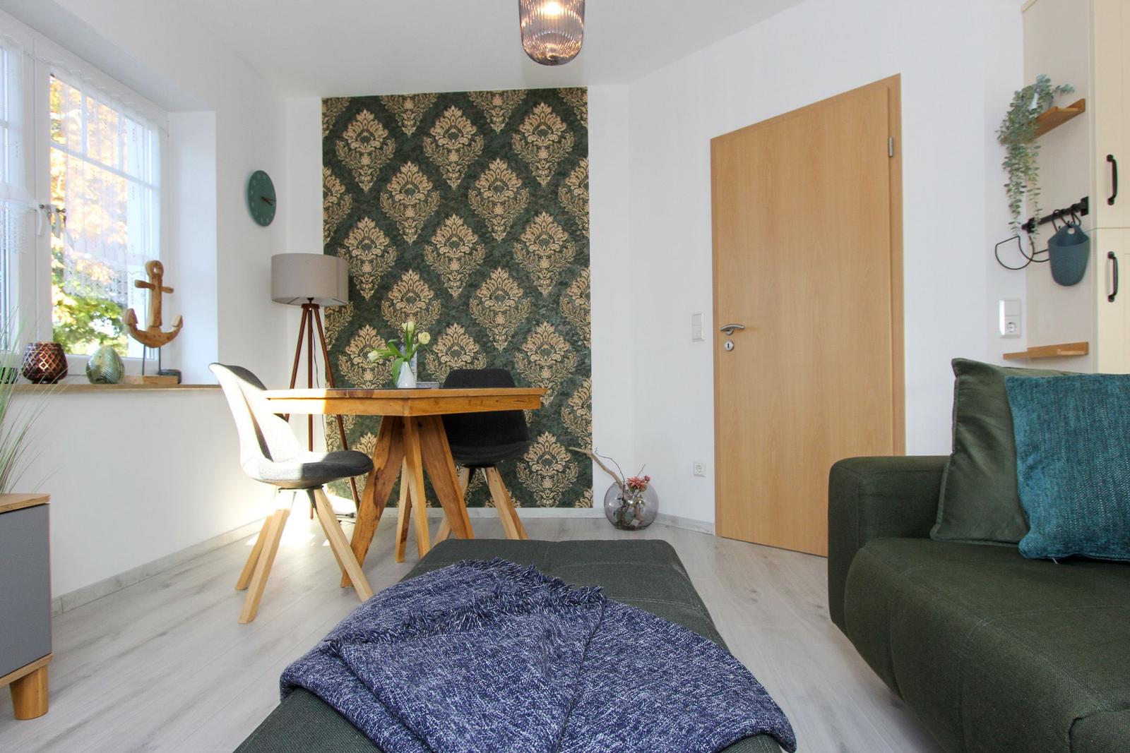Wohnzimmer mit Sofa, Esstisch und dekorativer Wandtapete.