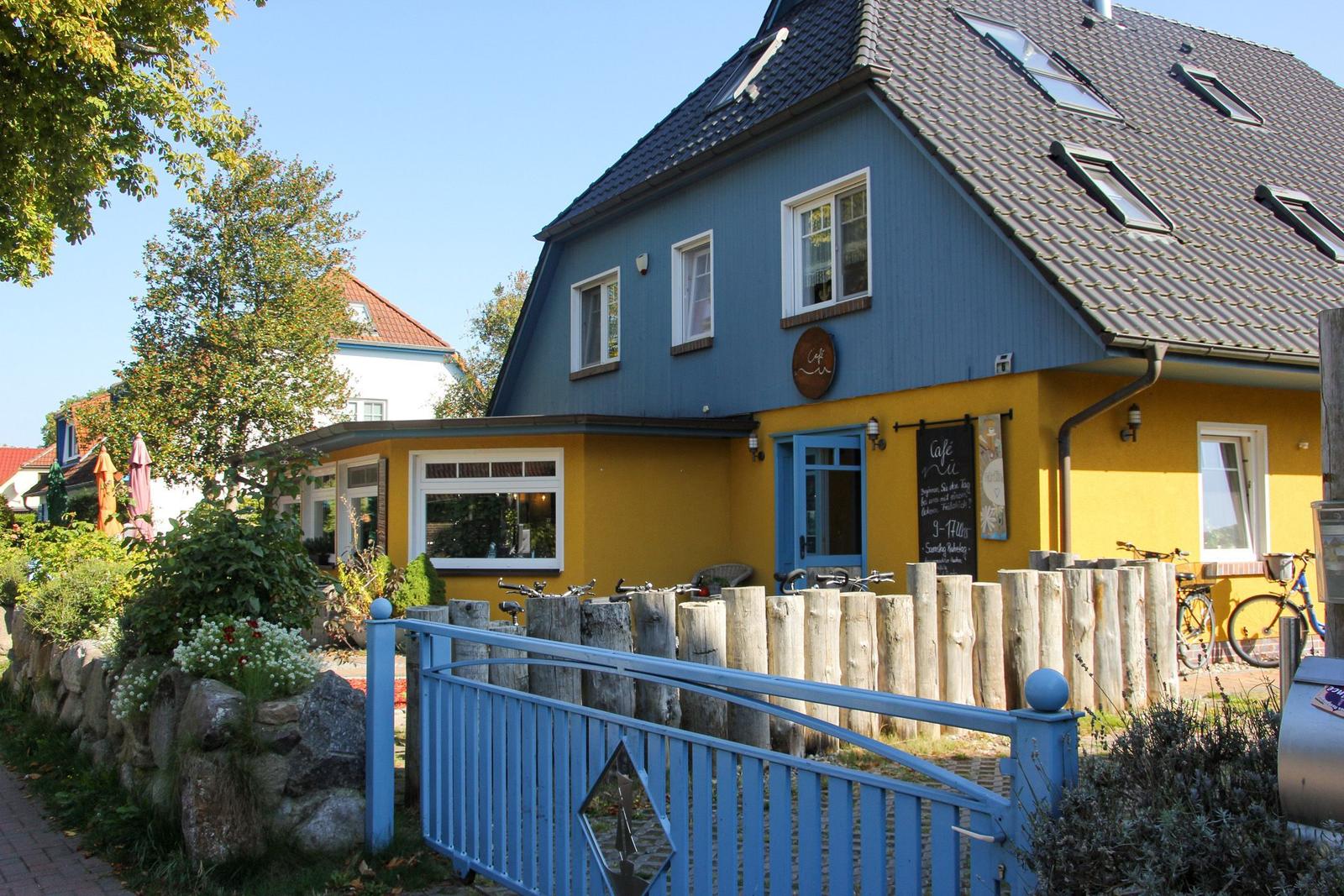 Ein zweistöckiges Haus mit blau-gelber Fassade, Dachfenstern und einem blauen Tor. Fahrräder stehen vor dem Gebäude.