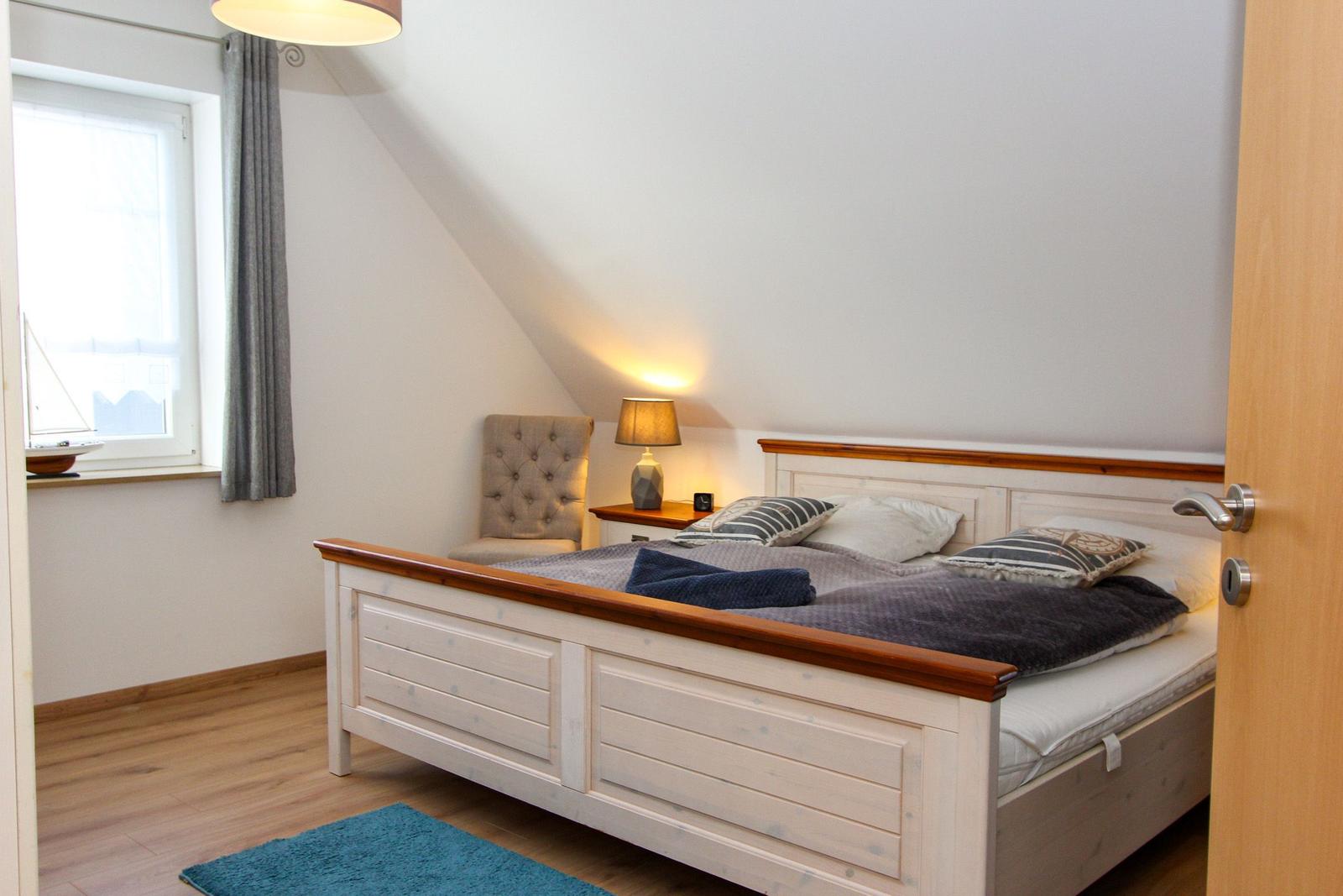 Schlafzimmer mit Bett, Nachttisch, Stuhl und Fenster.