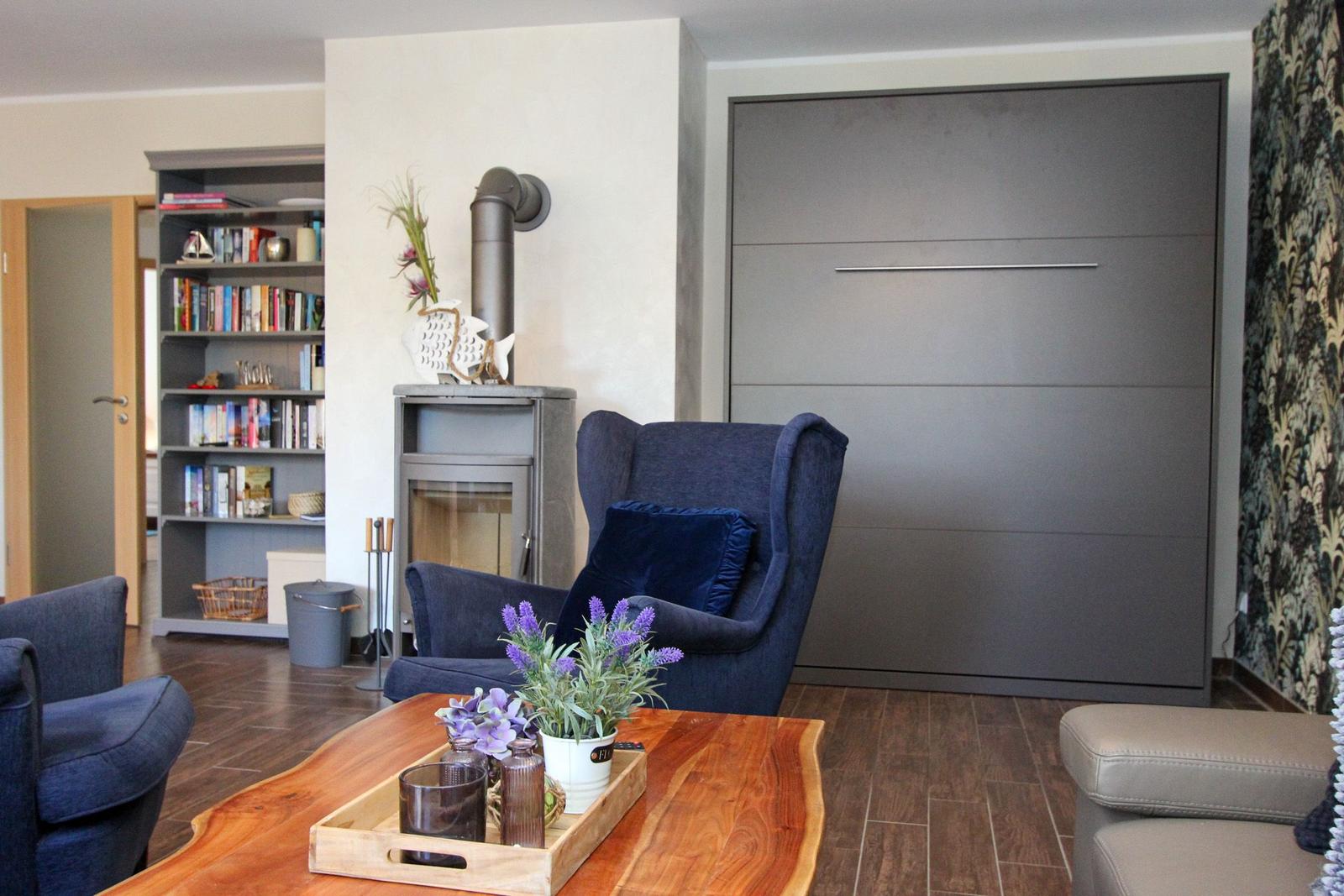 Wohnzimmer mit Sitzgelegenheiten, Kamin und Bücherregal. Holztisch mit Pflanzen.