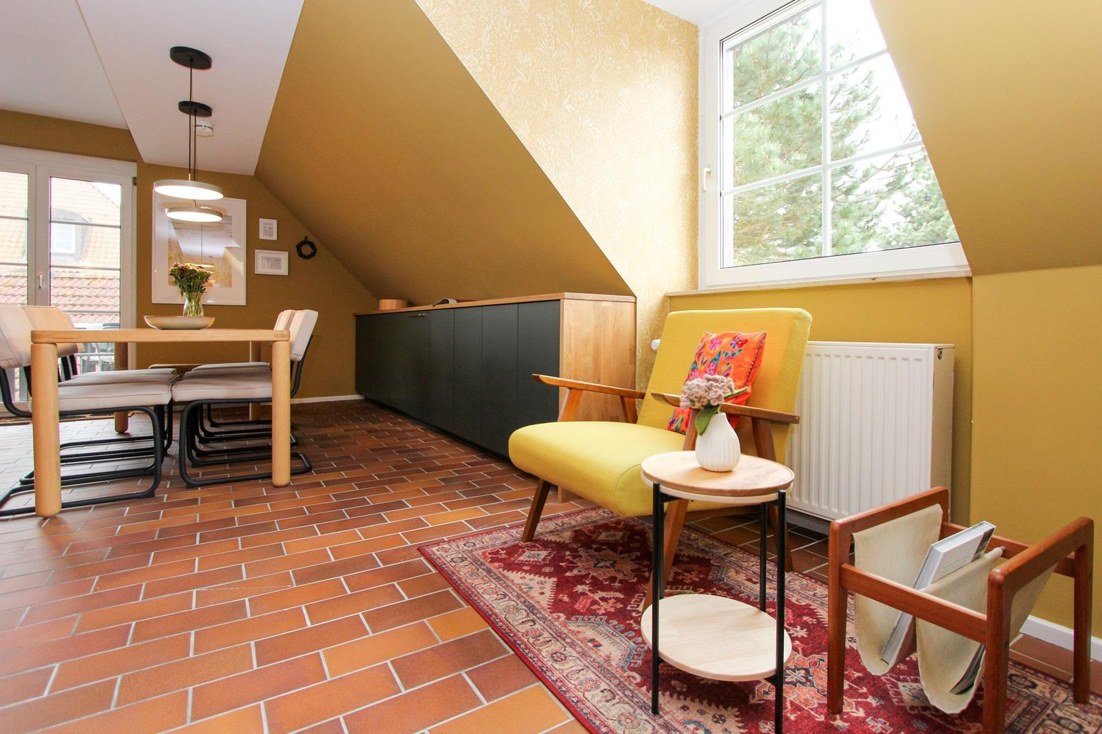 Wohn- und Essbereich mit gelbem Sessel, Holztisch und Terrakottaboden unter schrägem Dach.