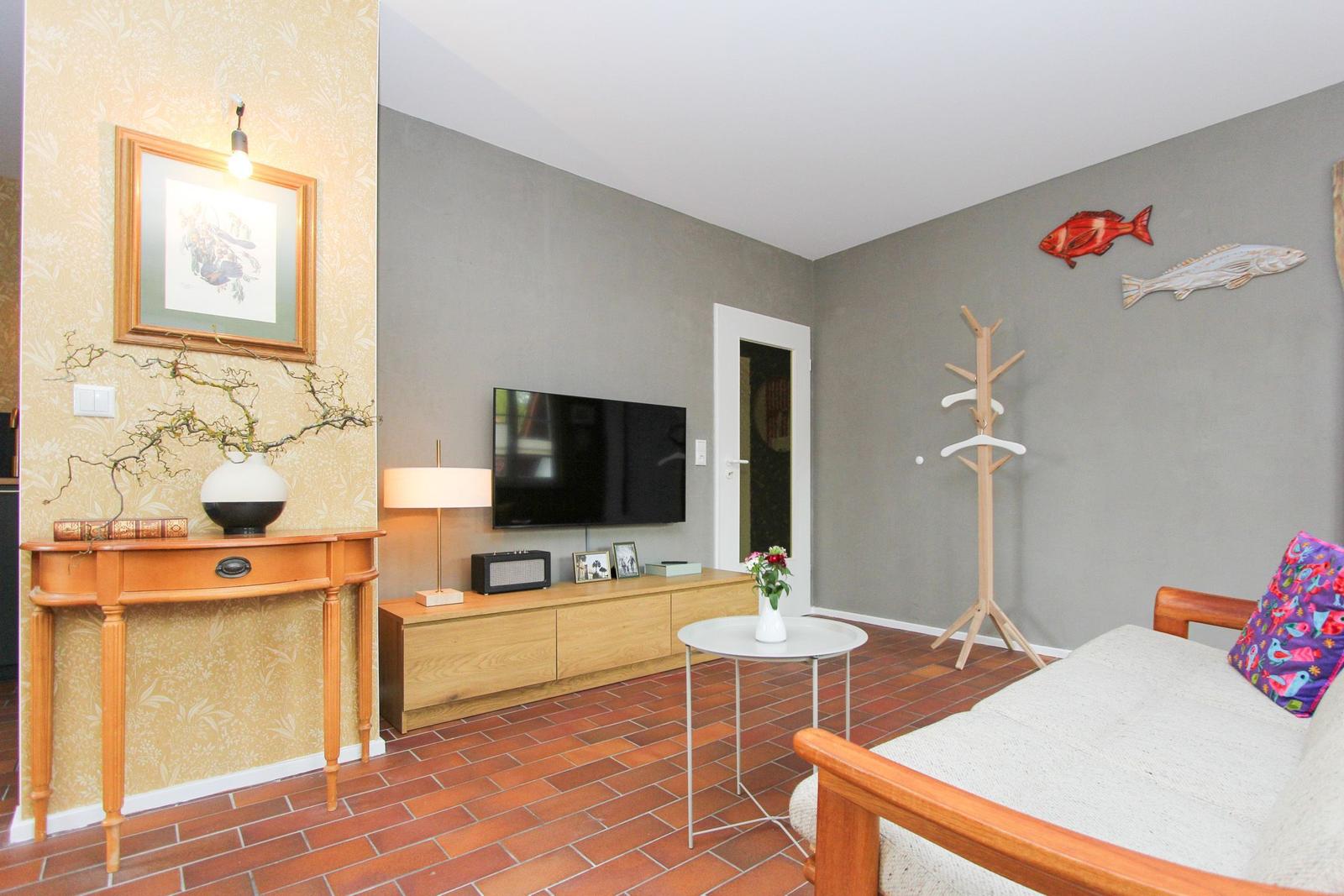 Wohnzimmer mit Fernseher, Couch, Kleiderständer und Wanddekoration