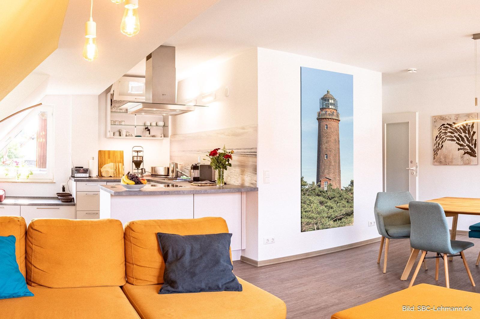 Wohnküche mit Sofa, Esstisch und Leuchten. Wandbild zeigt einen Leuchtturm.