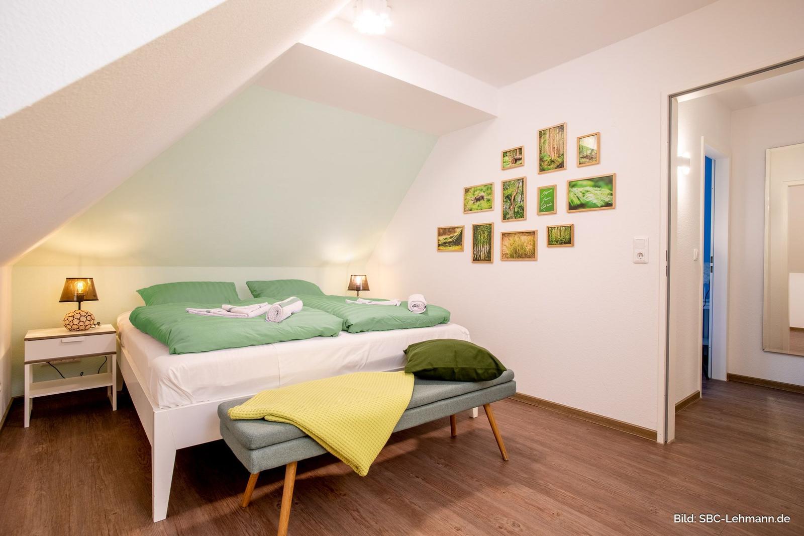 Schlafzimmer mit Doppelbett, grüner Bettwäsche und Holzboden unter schrägem Dach