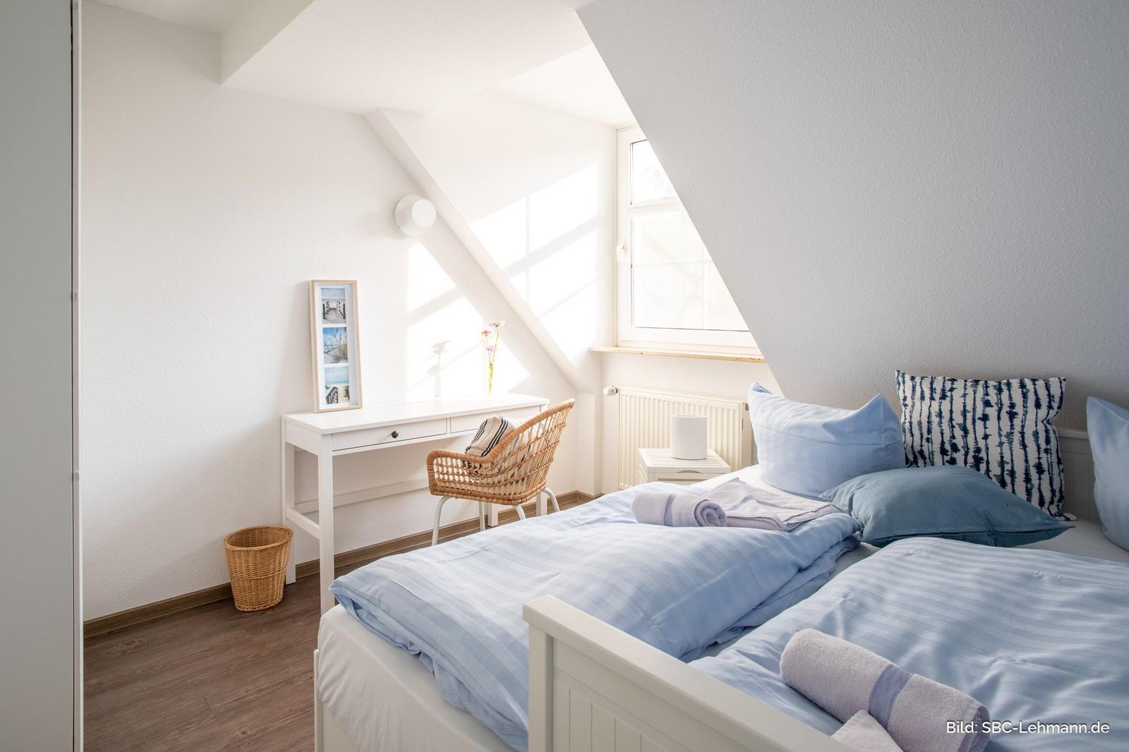 Zimmer mit Doppelbett, Schreibtisch und Fenster unter Dachschräge.