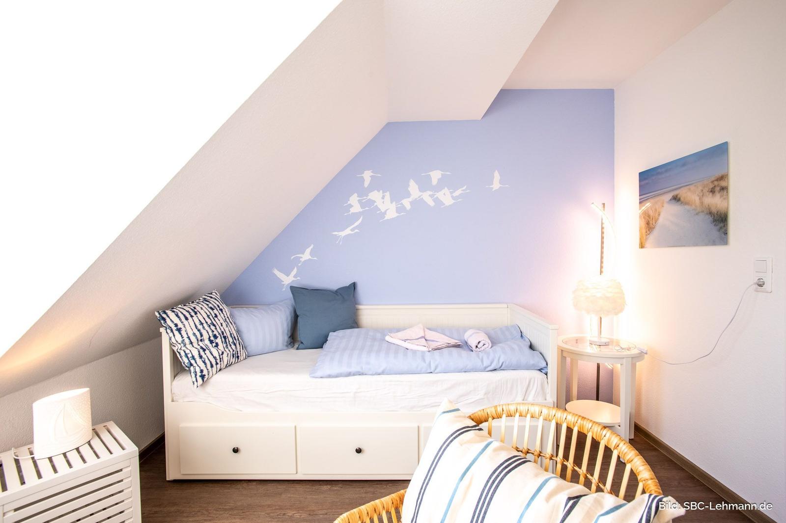 Schlafzimmer mit Dachschrägen, Bett mit Kissen und Wanddekoration.
