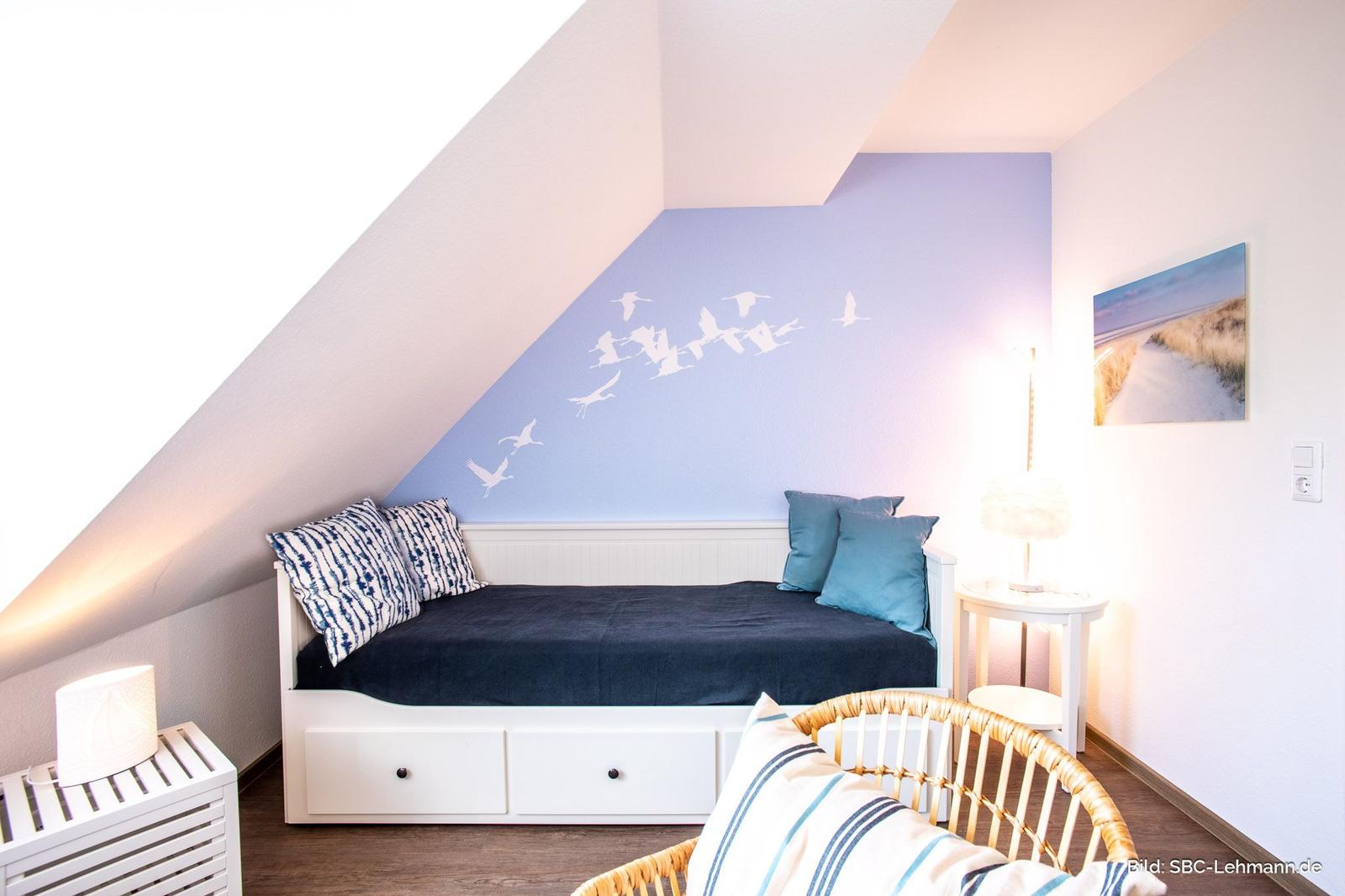 Schlafzimmer mit Dachschrägen, Bett mit Kissen und Wanddekoration.