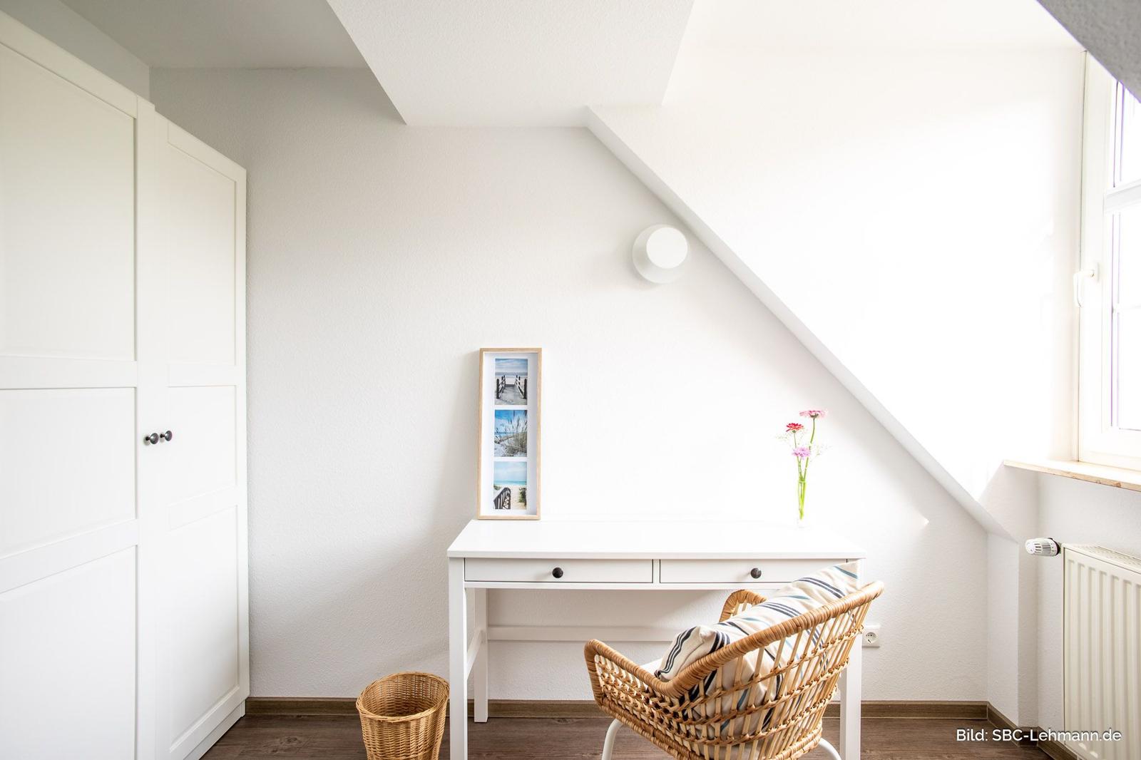 Ein Arbeitszimmer mit Schreibtisch, Stuhl und Kleiderschrank unter Dachschrägen.