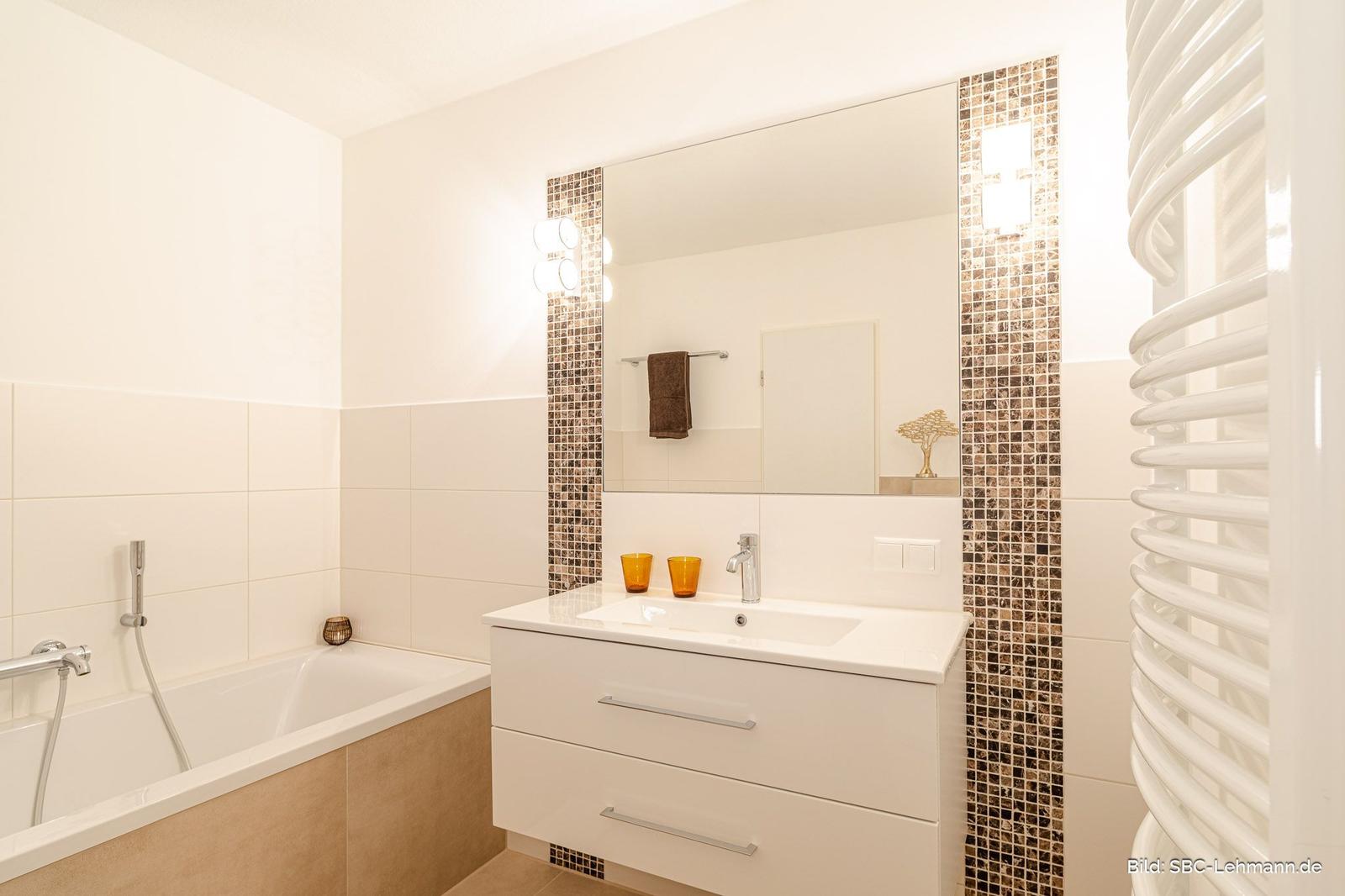 Badezimmer mit Badewanne, Waschtisch und Spiegel mit Mosaikrahmen.