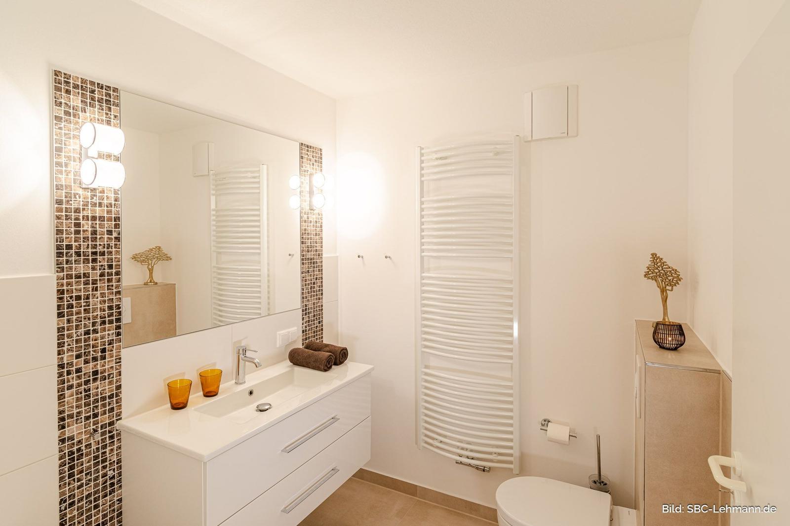 Badezimmer mit Waschbecken, Spiegel, Heizkörper und Toilette.