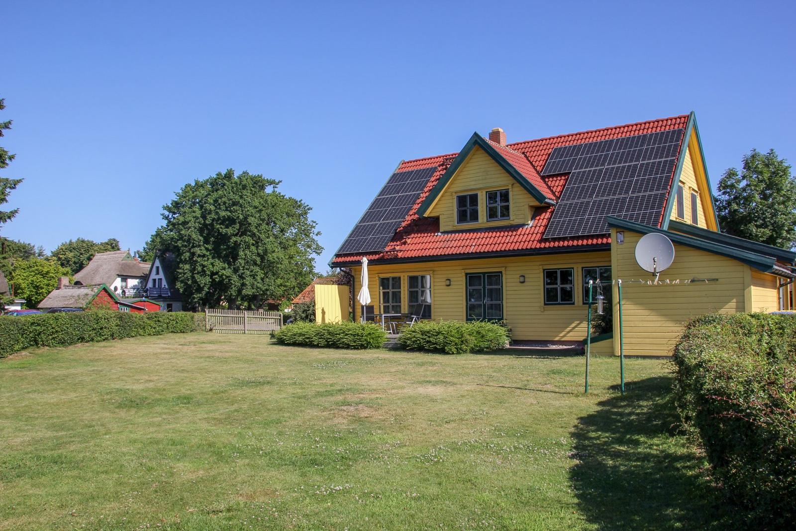 Gelbes Haus mit rotem Dach und Solarpaneelen. Garten mit Rasen und Sträuchern.