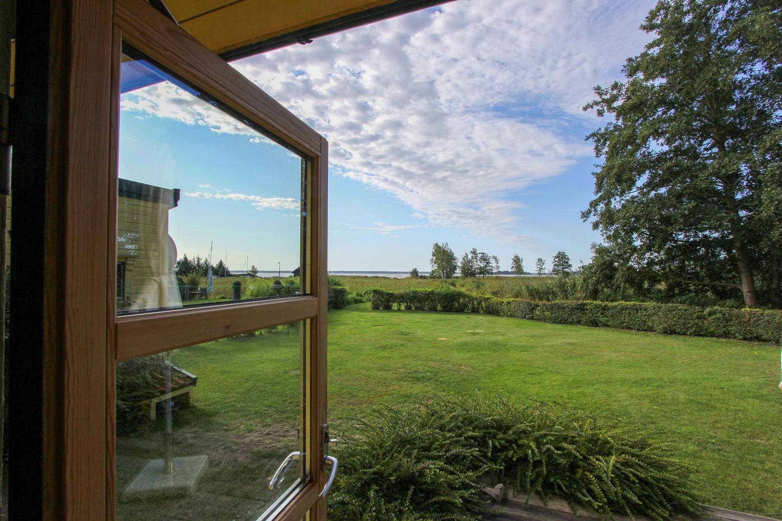 Durch das Fenster blickt man auf einen grünen Garten und einen See.