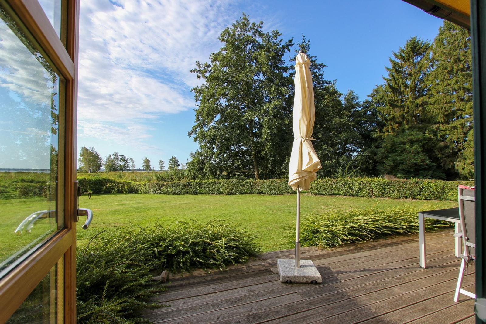 Terrasse mit Sonnenschirm, Blick auf grünen Garten und Bäume.