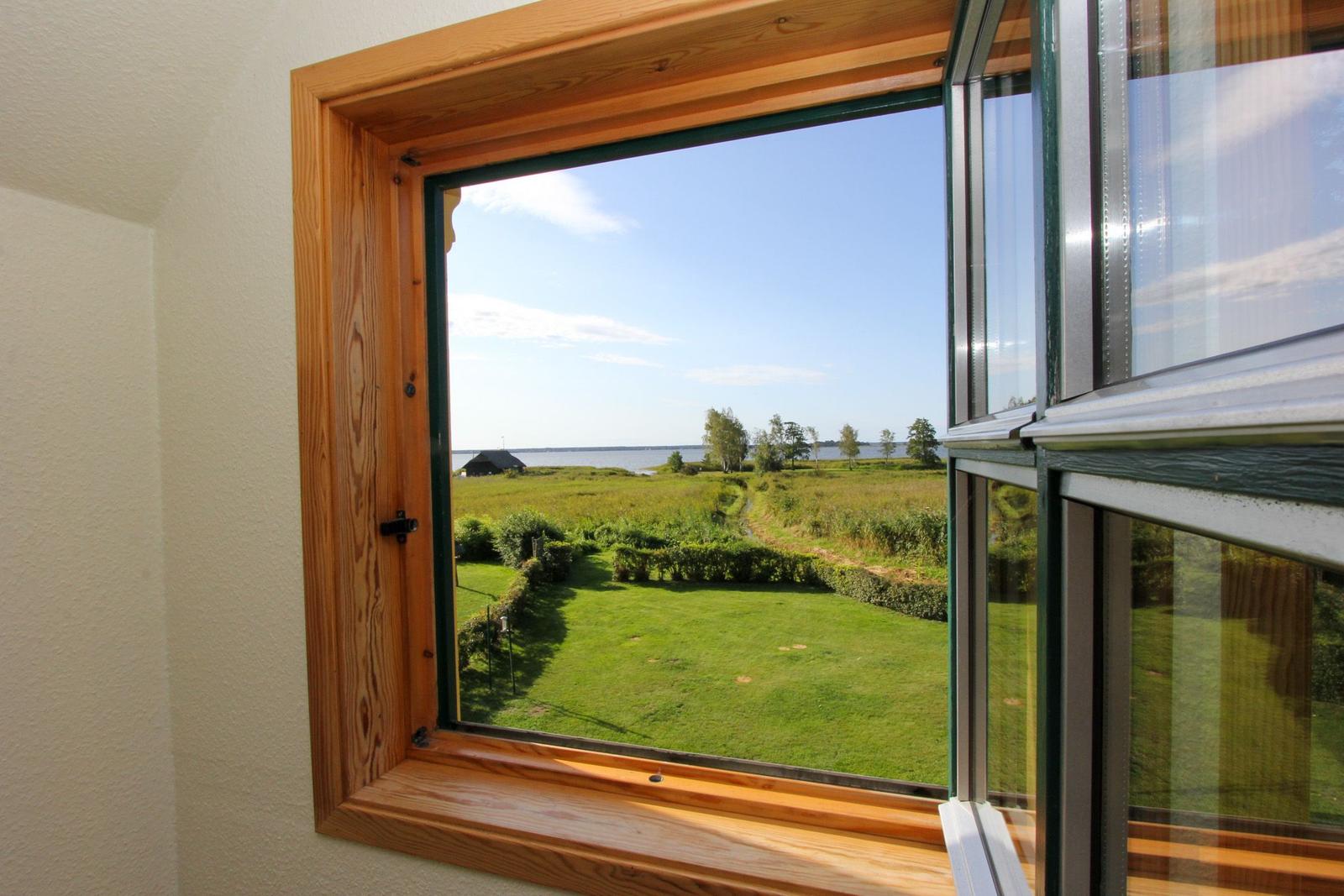Durch das Fenster blickt man auf eine grüne Wiese und einen See.