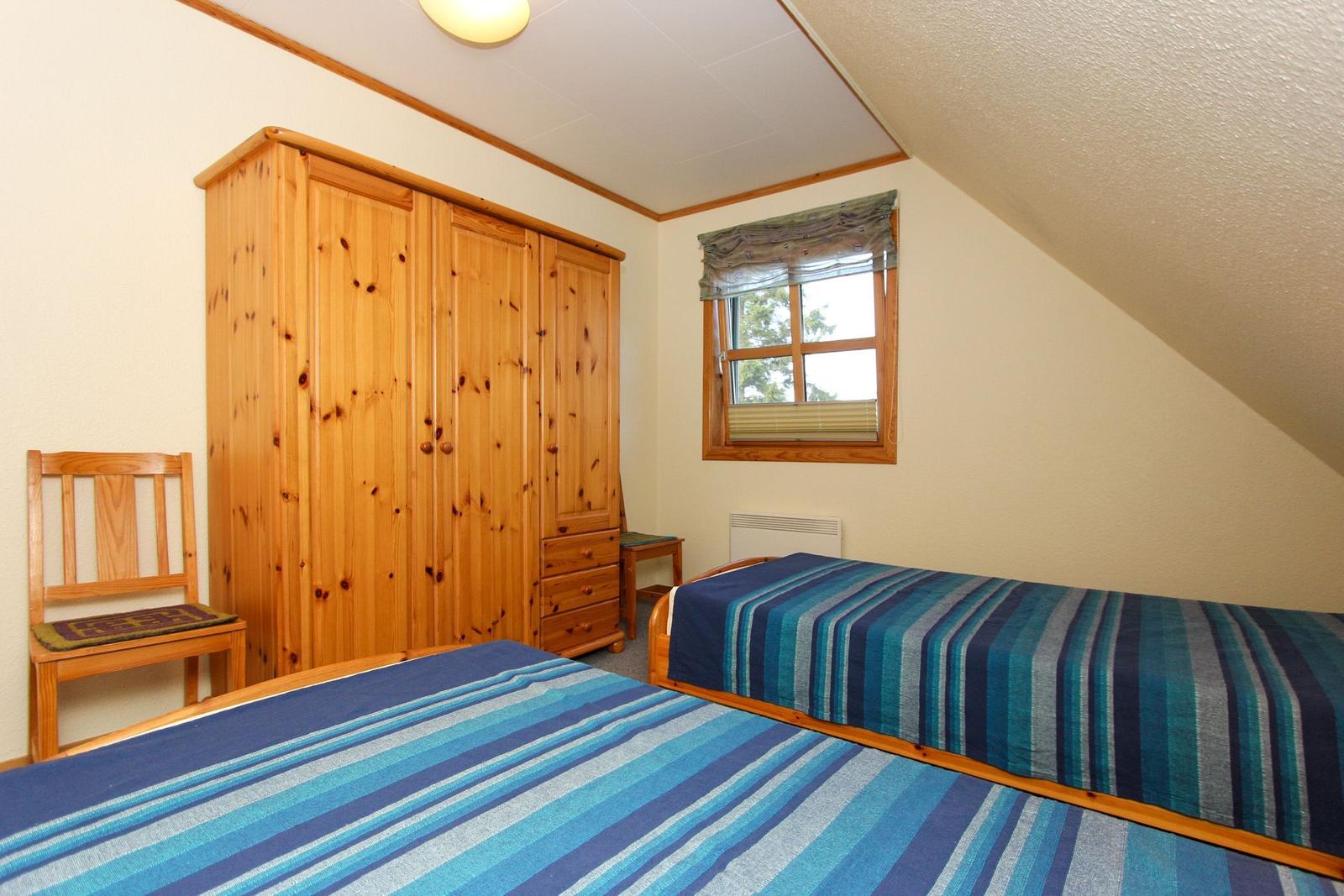 Zimmer mit zwei Betten, Holzschrank und Fenster mit Blick auf Bäume.