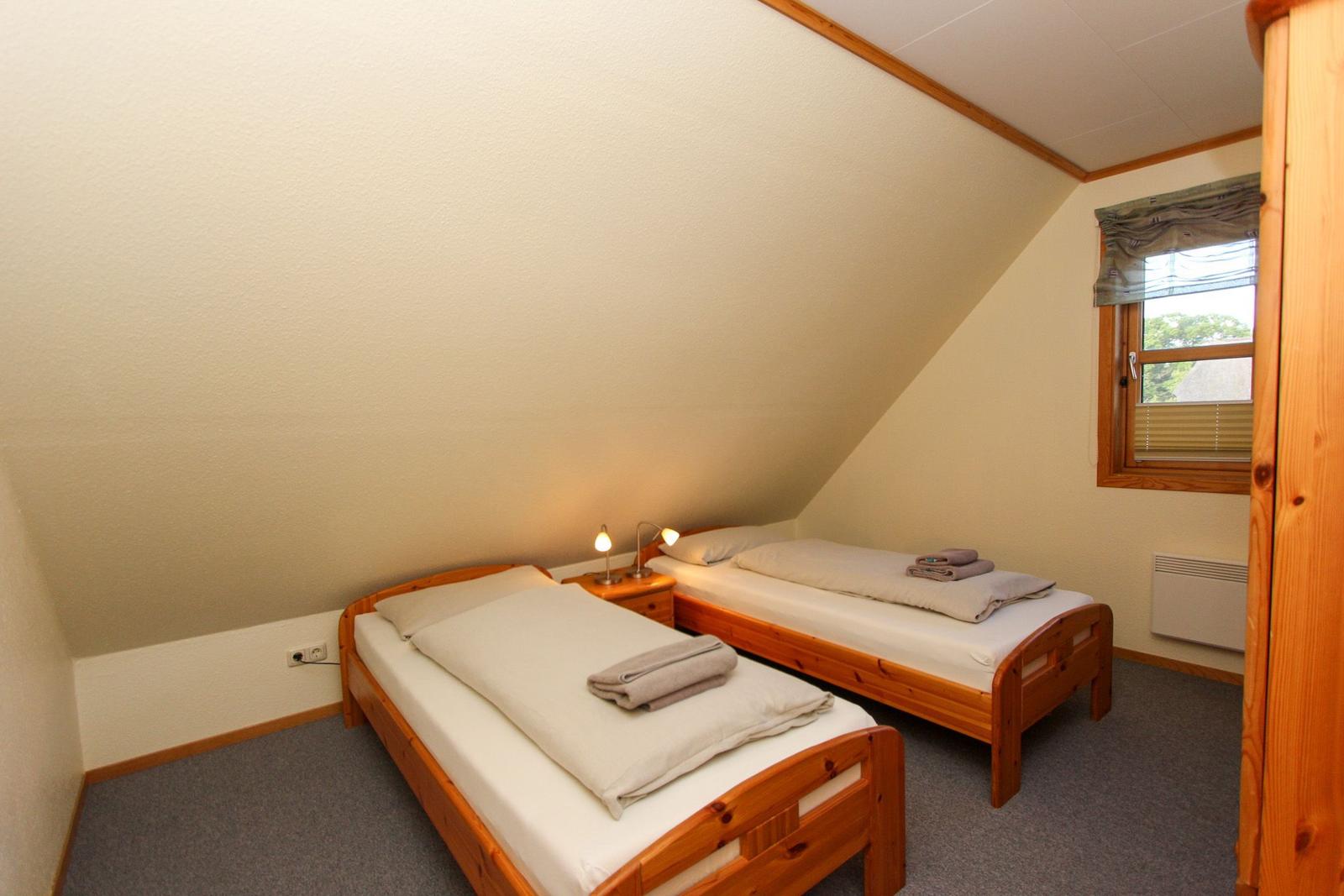 Zwei Einzelbetten mit Holzrahmen, Fenster und Heizung im Dachgeschosszimmer.