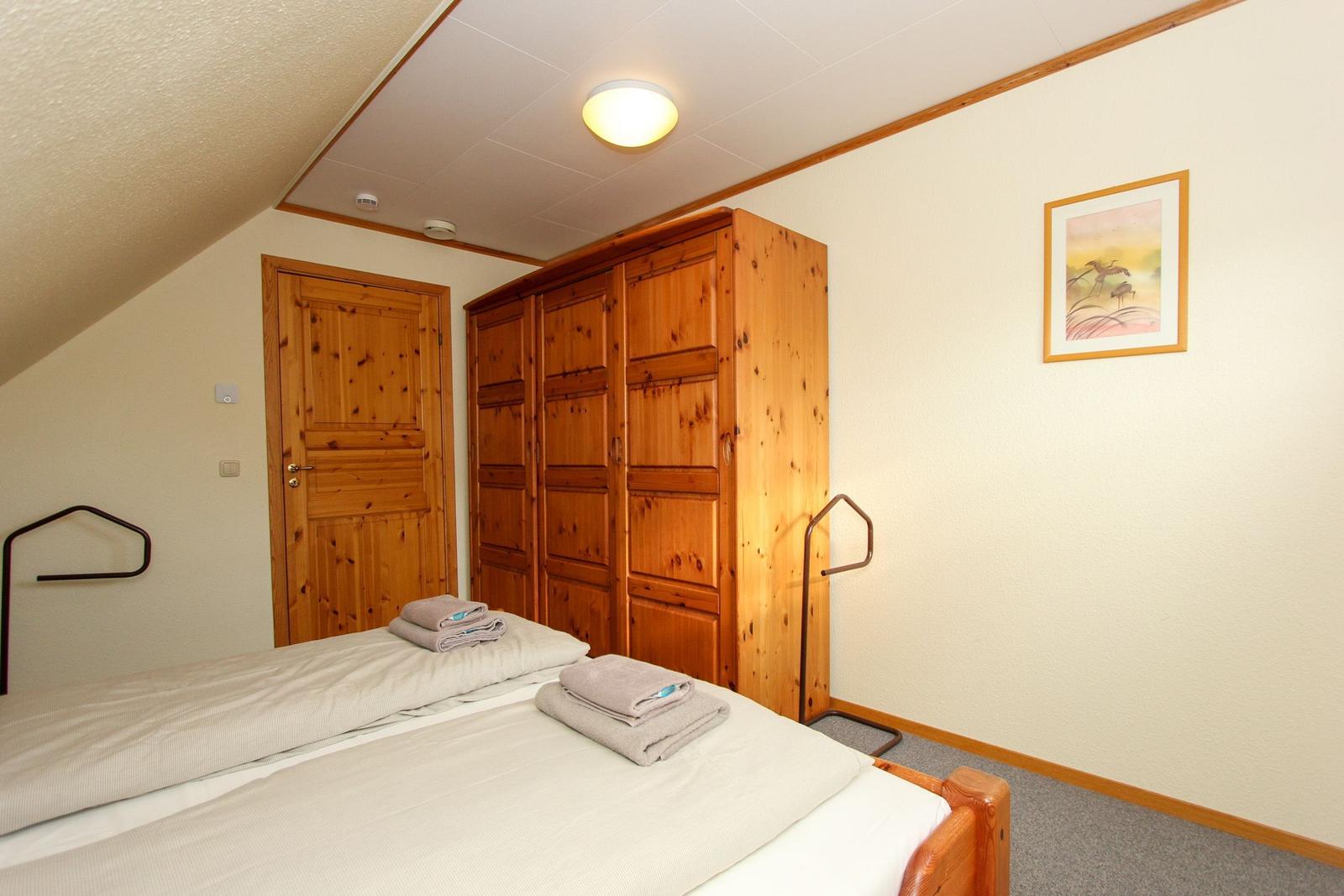 Schlafzimmer mit Holzbett, Kleiderschrank und Tür. Auf Bett liegen Handtücher.