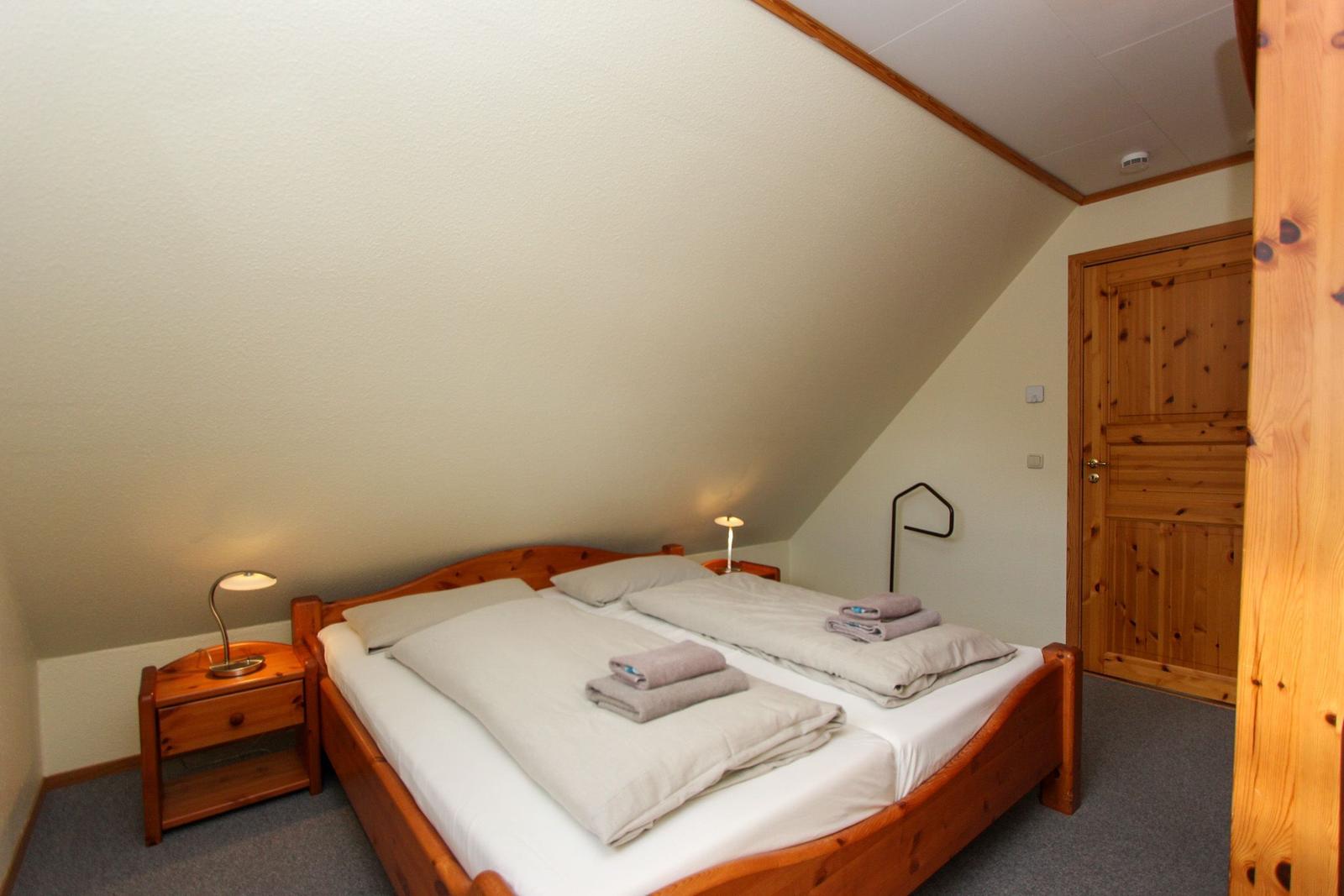 Schlafzimmer mit Holzbett, Nachttisch und Lampen unter schrägem Dach.