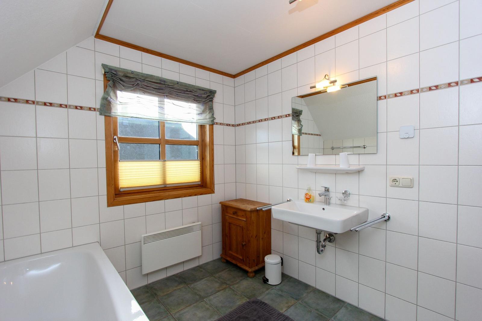 Badezimmer mit Badewanne, Waschbecken und Holzschrank. Fenster mit Jalousie und Heizkörper.