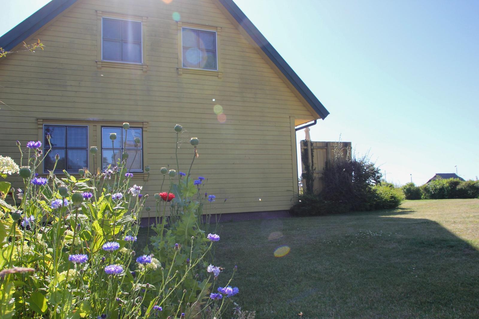 Gelbes Haus mit Garten und Blumen im Vordergrund unter blauem Himmel.