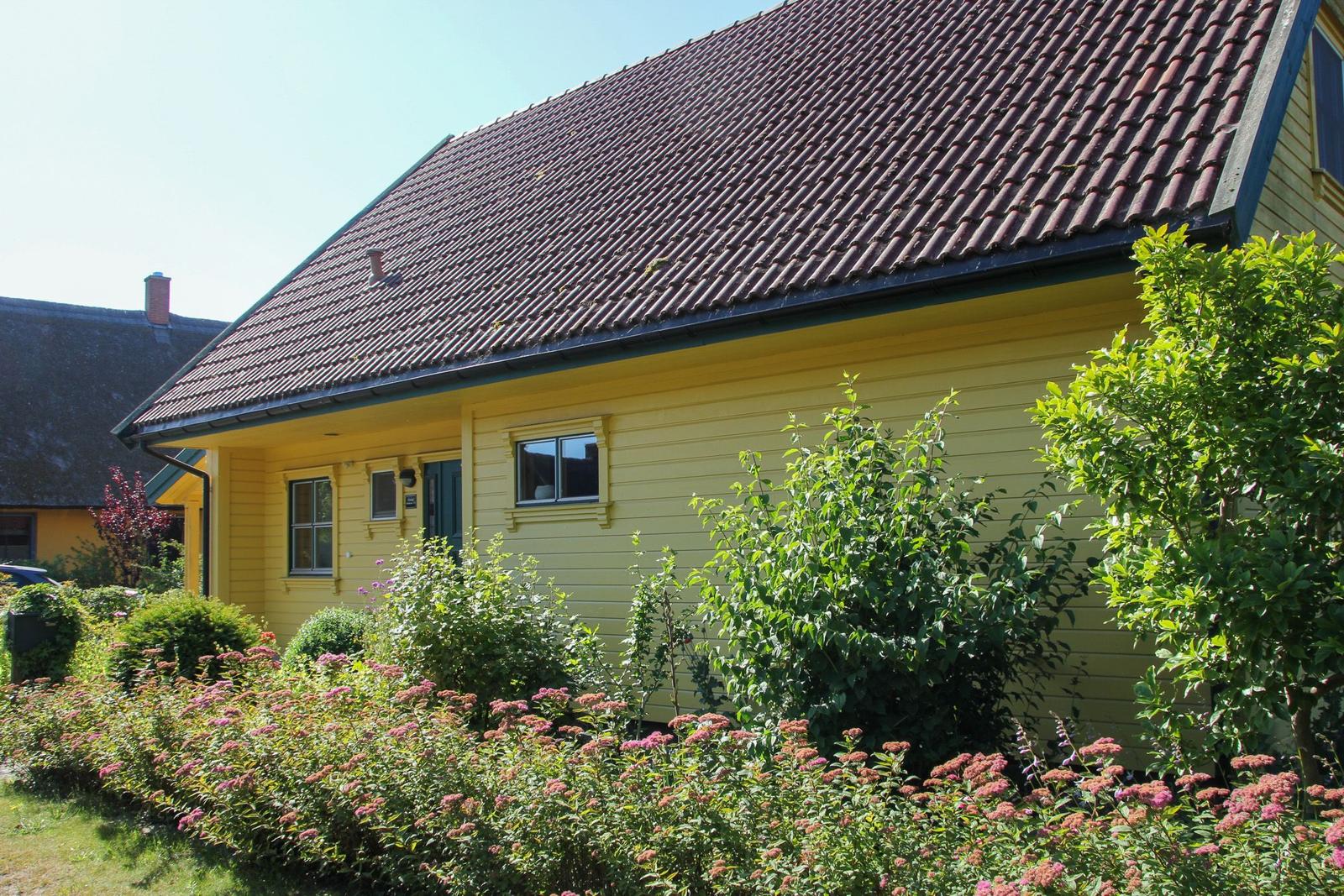 Gelbes Holzhaus mit rotem Dach und grüner Umgebung.