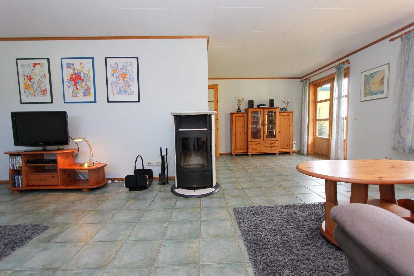 Wohnzimmer mit Kamin, TV und Holzmöbel. Fenster mit Vorhängen. Fliesenboden und Teppich.