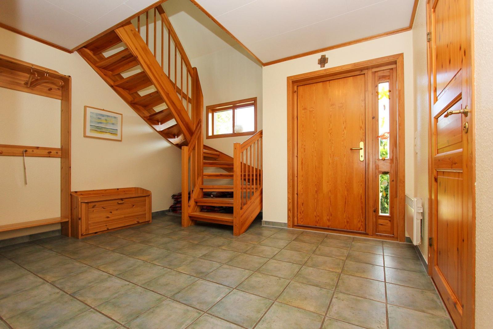 Eingangsbereich mit Holztreppe, Tür und Holzbank. Fliesenboden und Wandgestaltung.