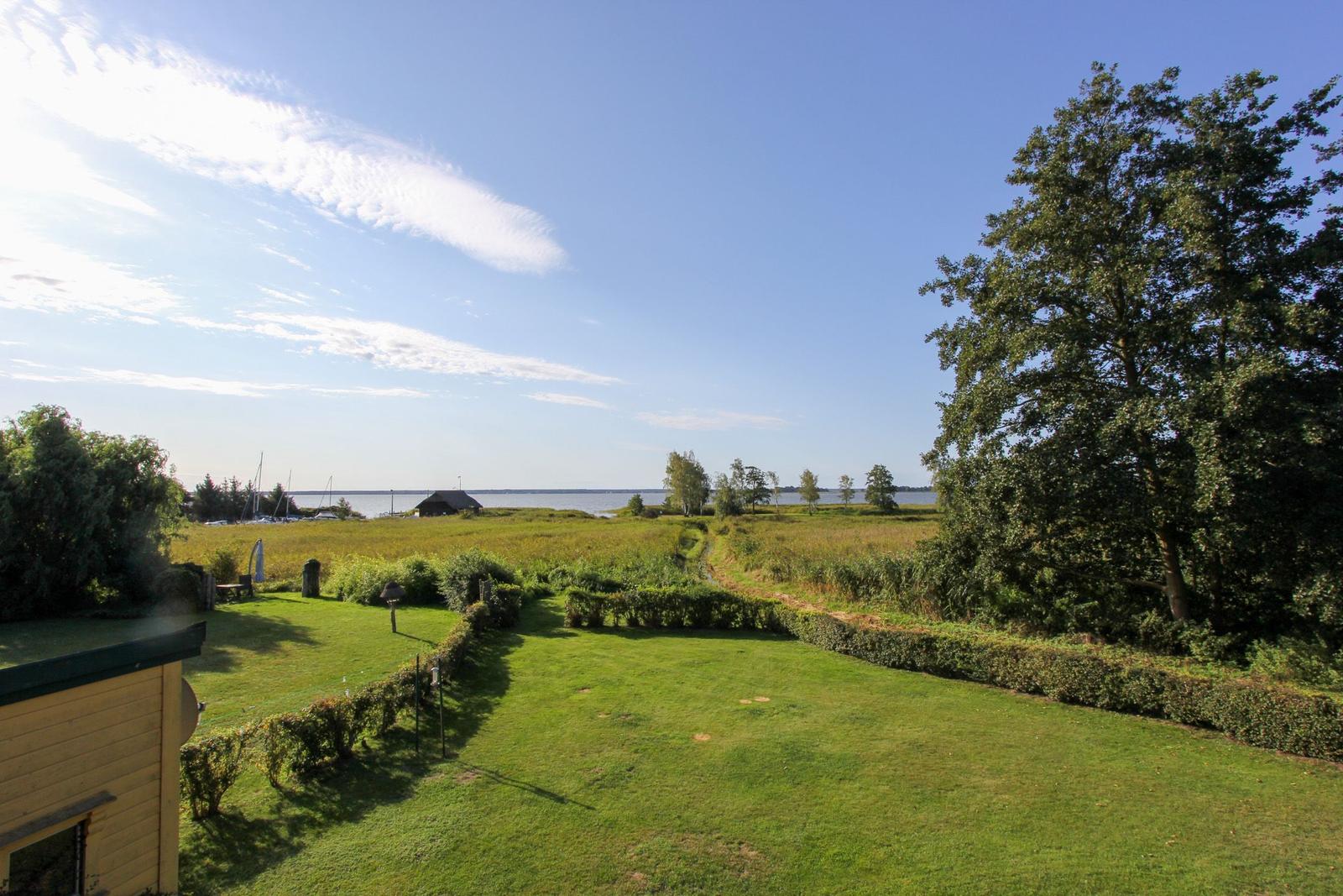Grüner Garten mit Blick auf Wasser und Bäume unter blauem Himmel.