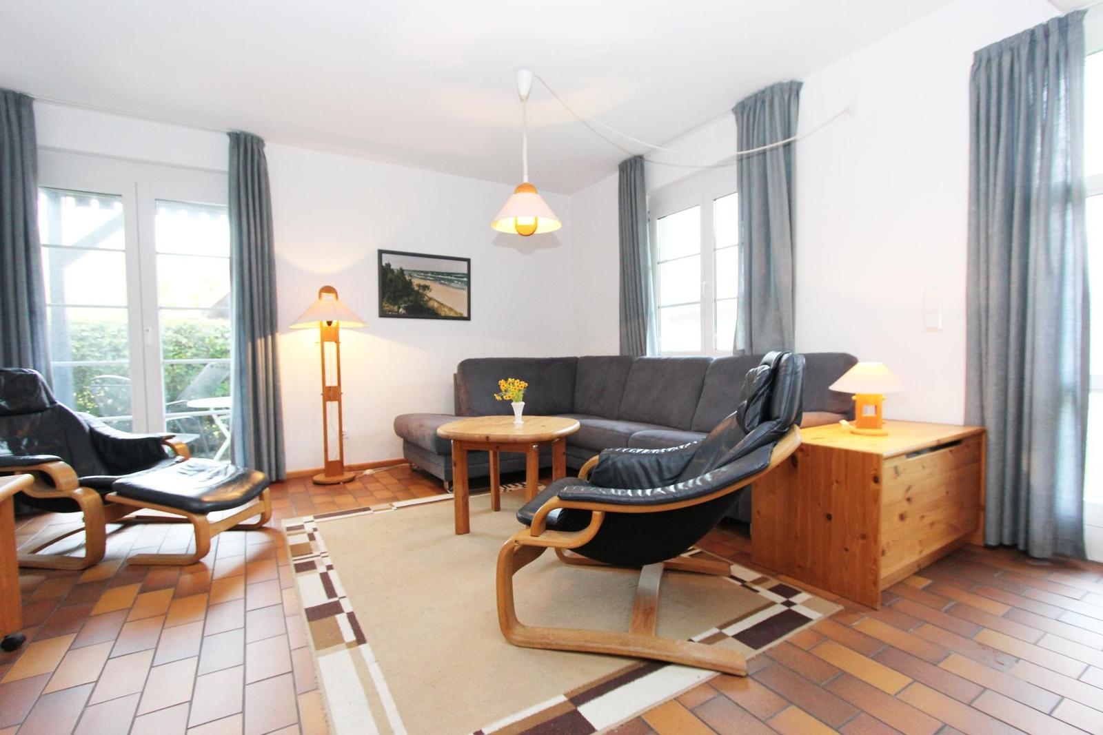 Wohnzimmer mit Sofa, zwei Sesseln, Tisch und Fenstern.