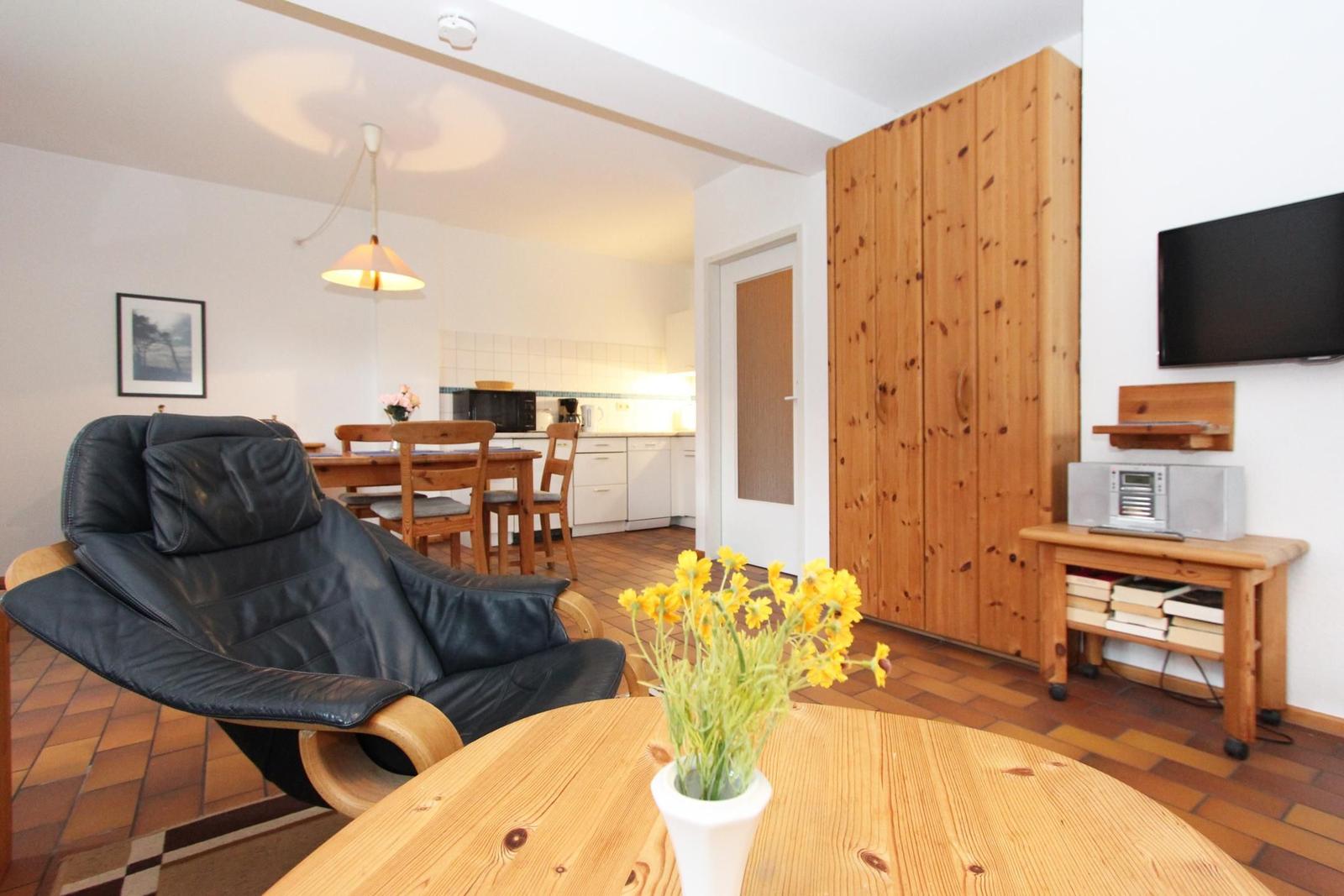 Wohnzimmer mit Essbereich, Holzmöbel und Fernseher. Im Vordergrund eine schwarze Relaxliege.