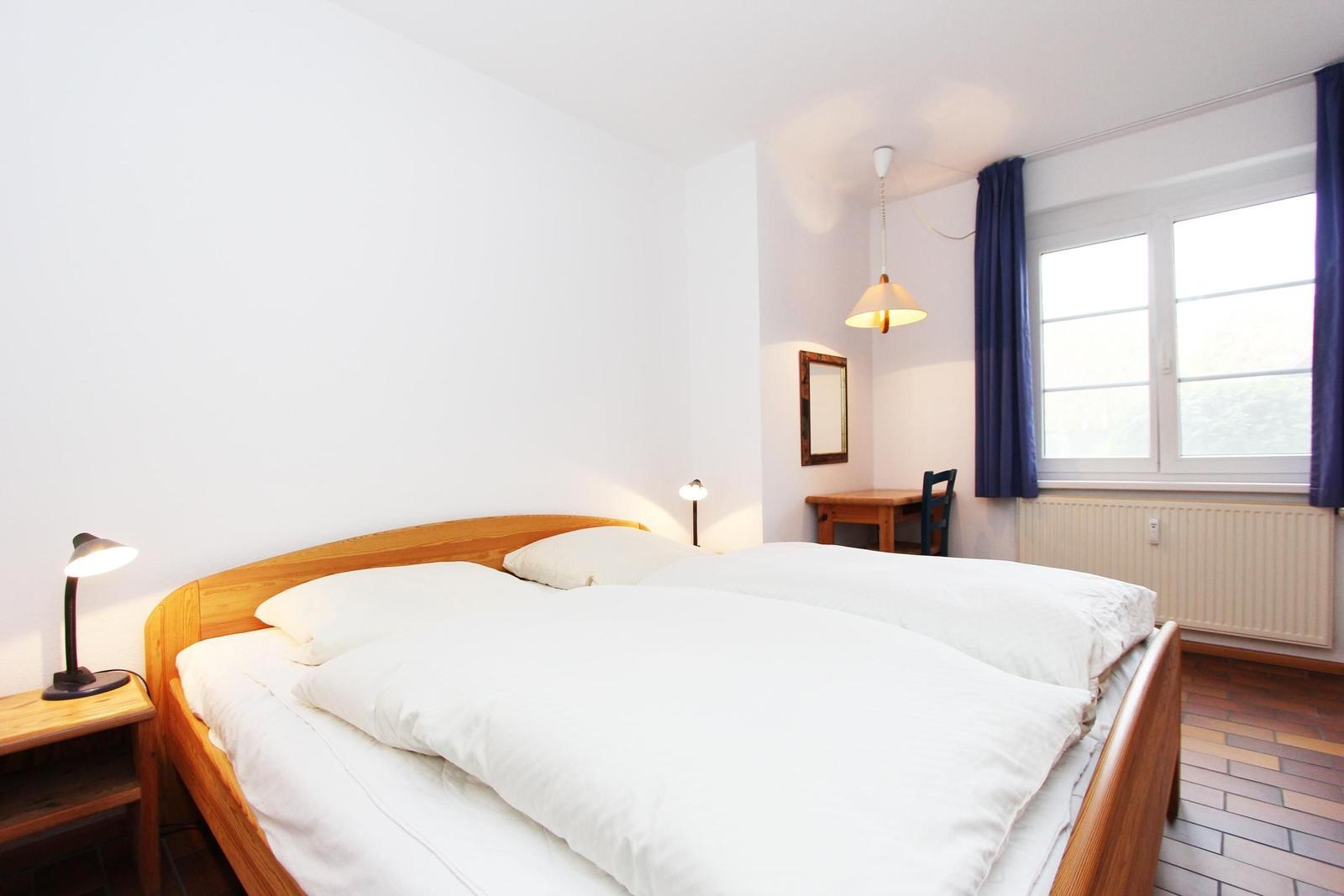 Ein Schlafzimmer mit Doppelbett, Schreibtisch und Fenster mit Vorhängen.