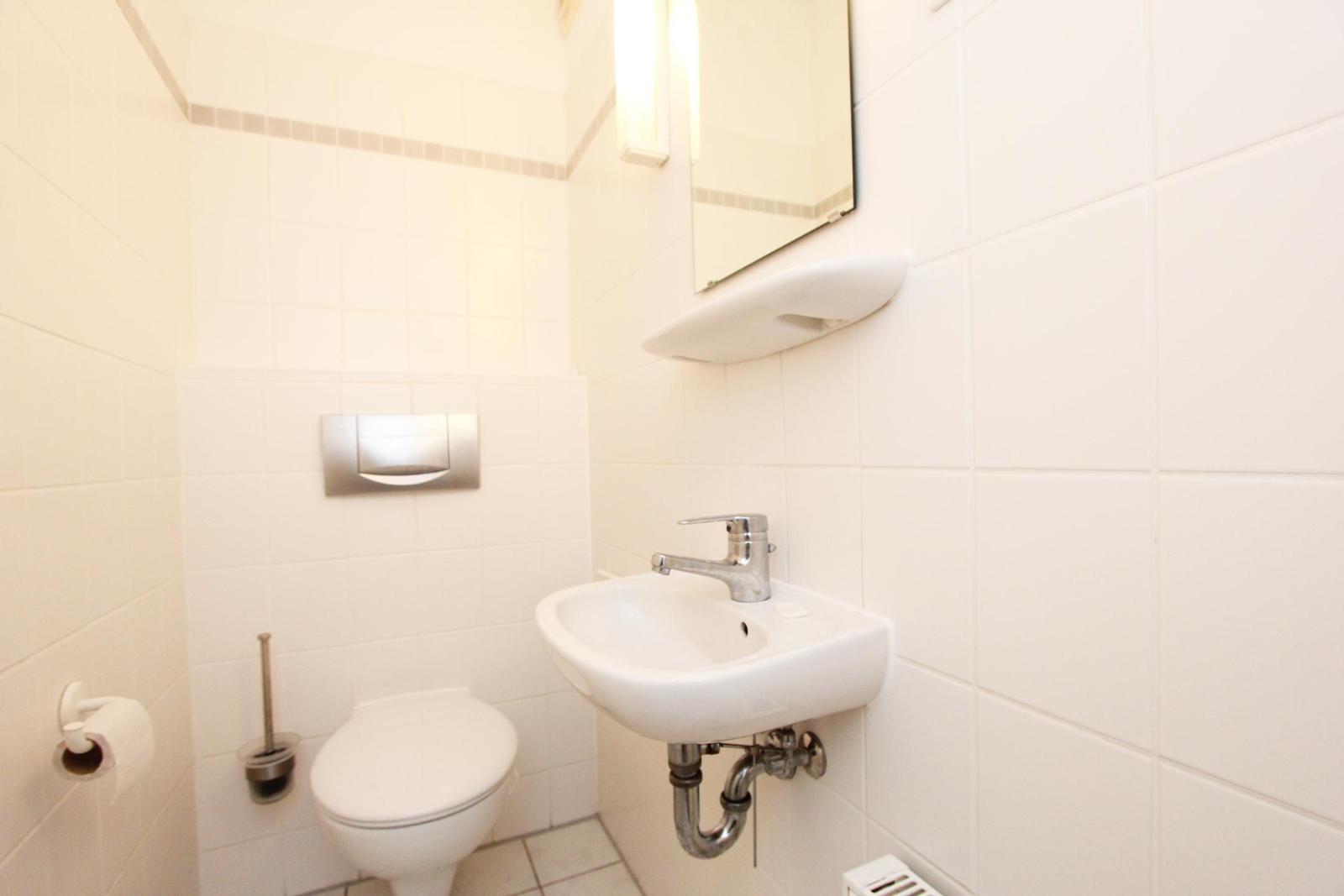 Badezimmer mit Toilette, Waschbecken und Spiegel an der Wand.