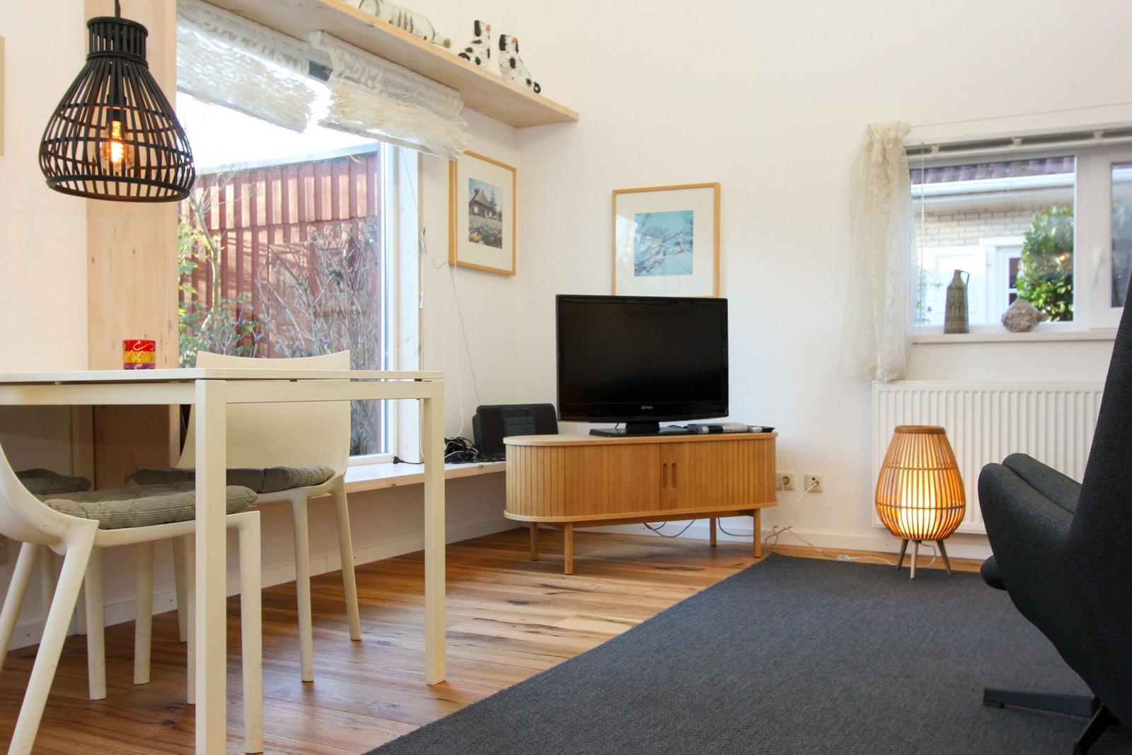Wohn- und Essbereich mit Holzboden, TV, Tisch, Stühlen und Lampen.