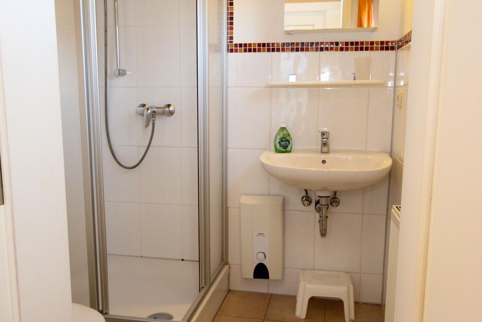 Badezimmer mit Dusche, Waschbecken und Spiegel.
