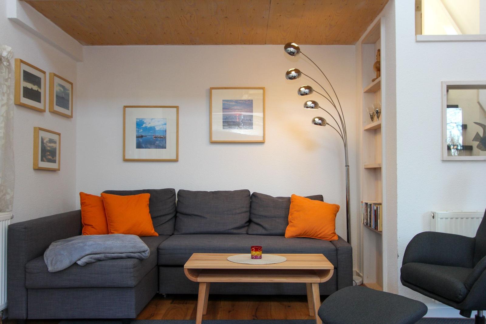 Ein Wohnzimmer mit grauem Sofa, orangefarbenen Kissen und einem Holztisch.