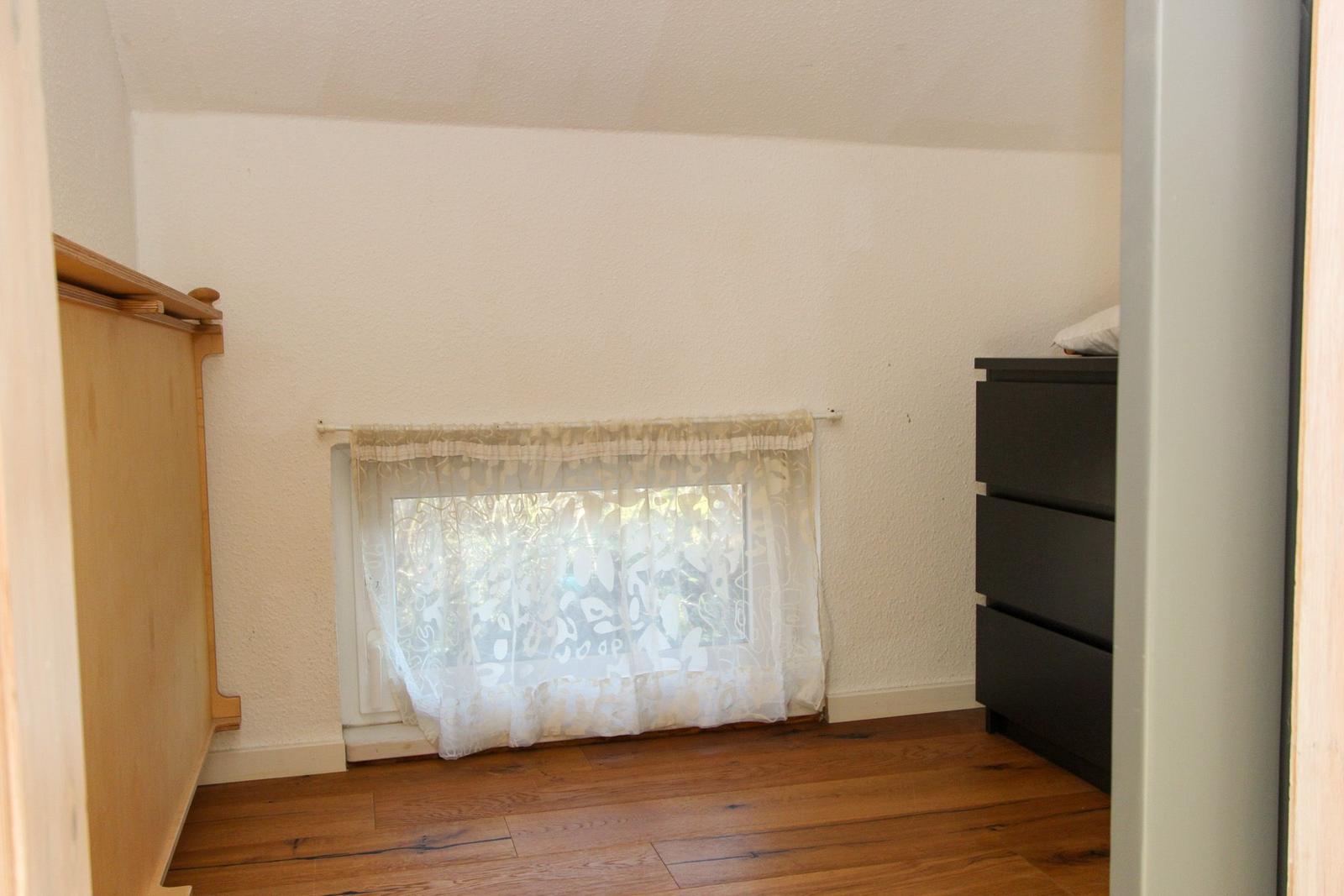 Zimmer mit Holzboden, Fenster mit Vorhang und Schrank.