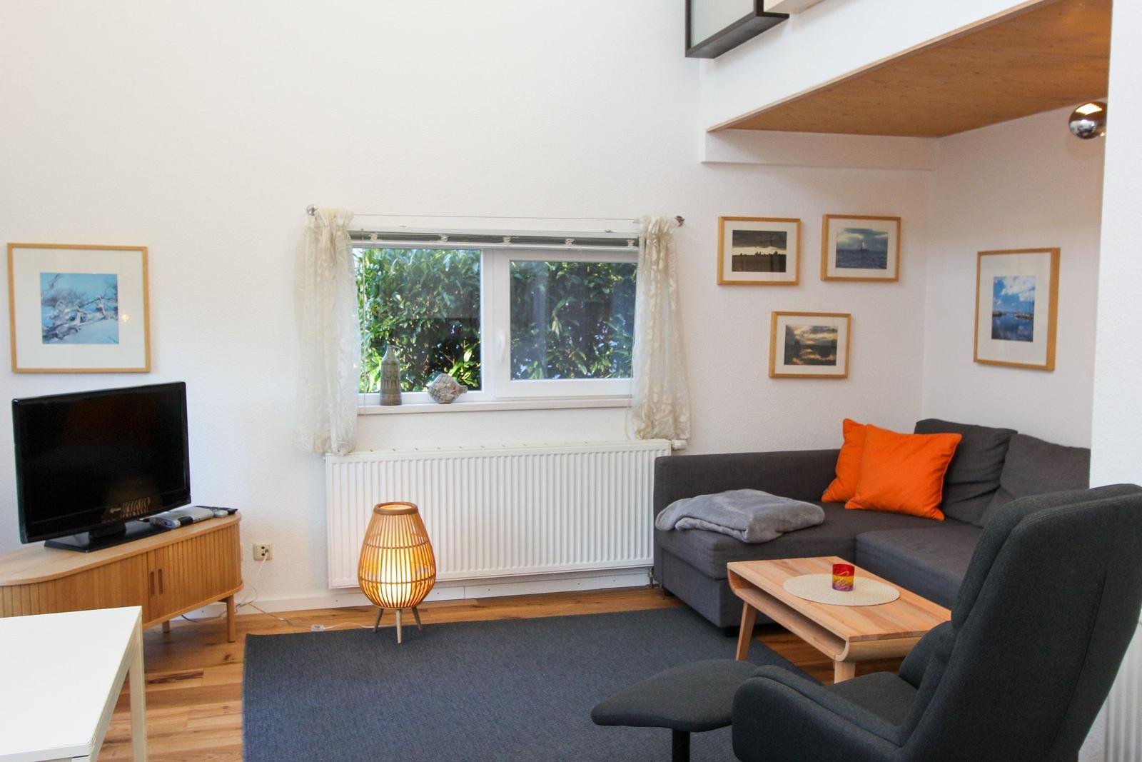 Wohnzimmer mit Sofa, Fernseher und Fenster mit Blick auf Grün.