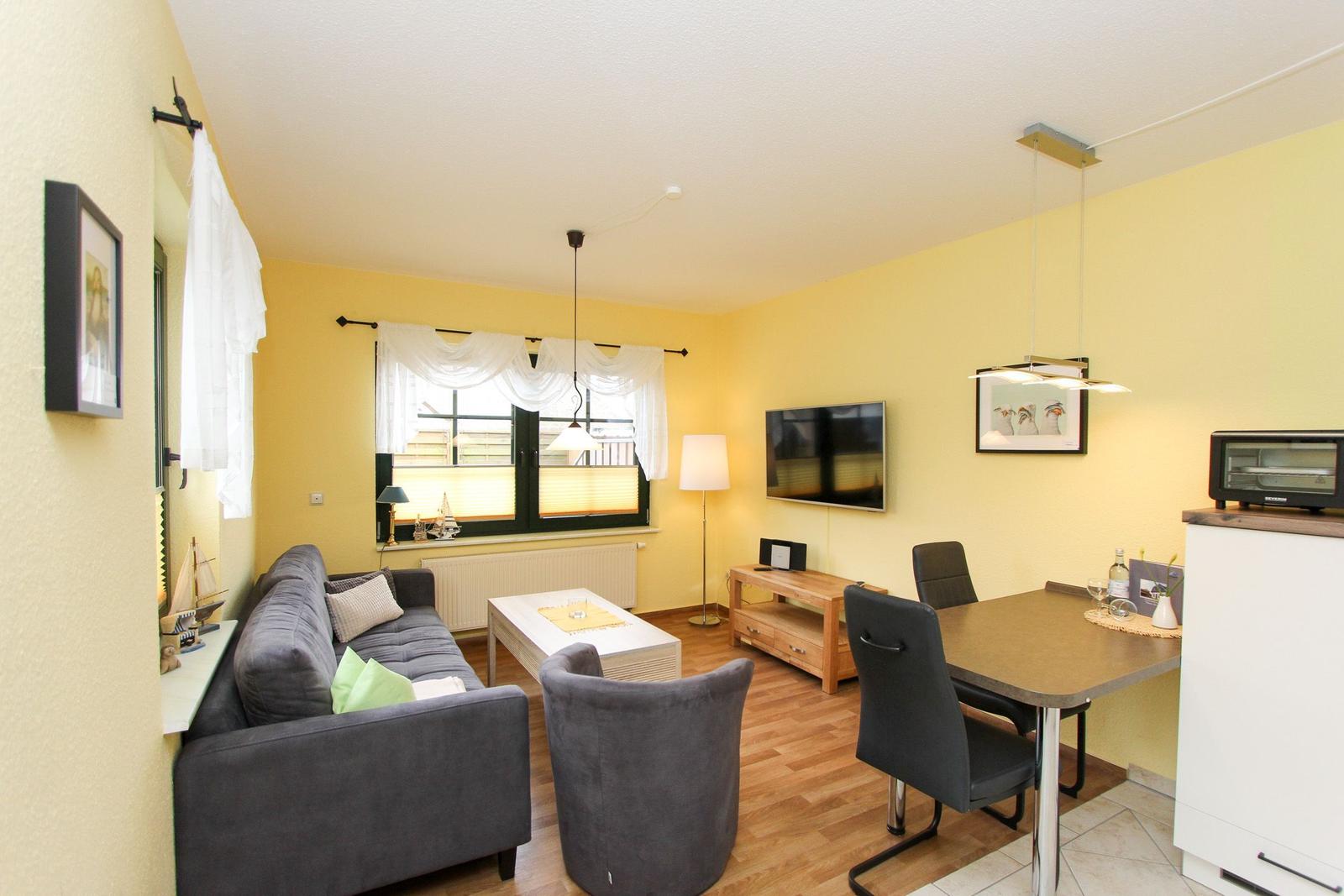 Wohnzimmer mit Sofa, Esstisch und Fernseher an gelben Wänden.