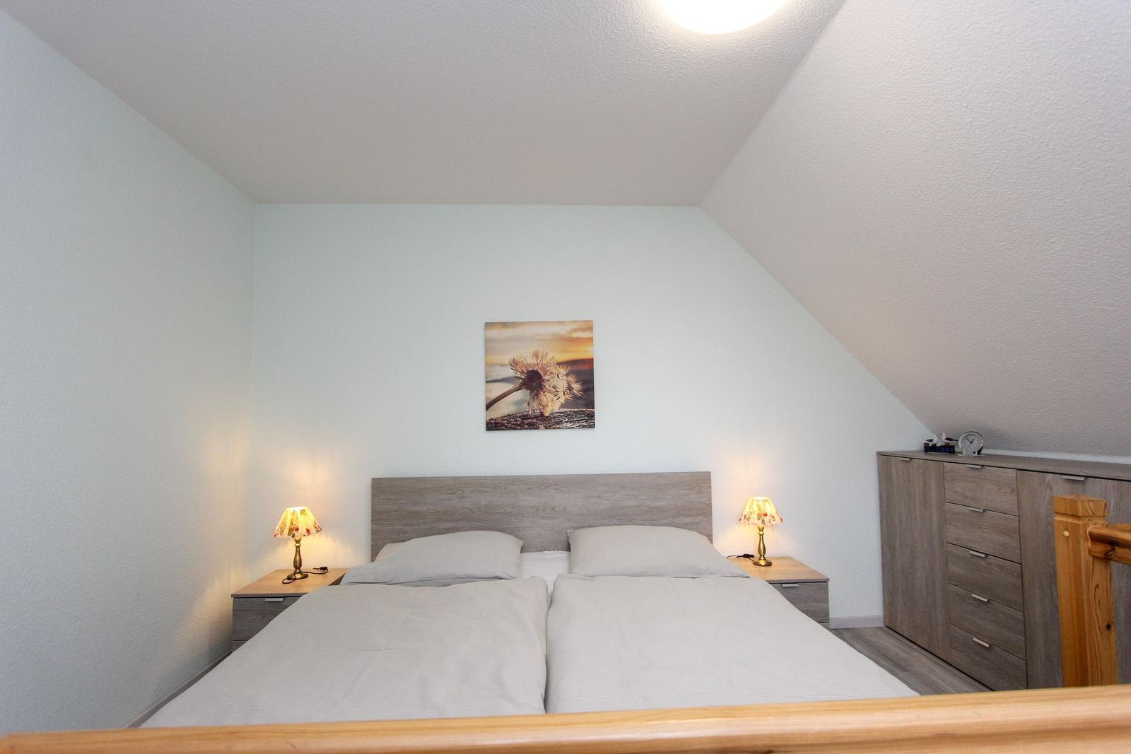 Schlafzimmer mit Doppelbett, Nachttischen und Schrank unter schräger Decke.