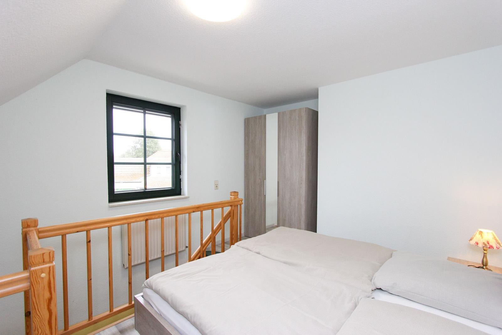 Schlafzimmer mit Doppelbett, Holzgeländer und Fenster mit Blick nach außen.