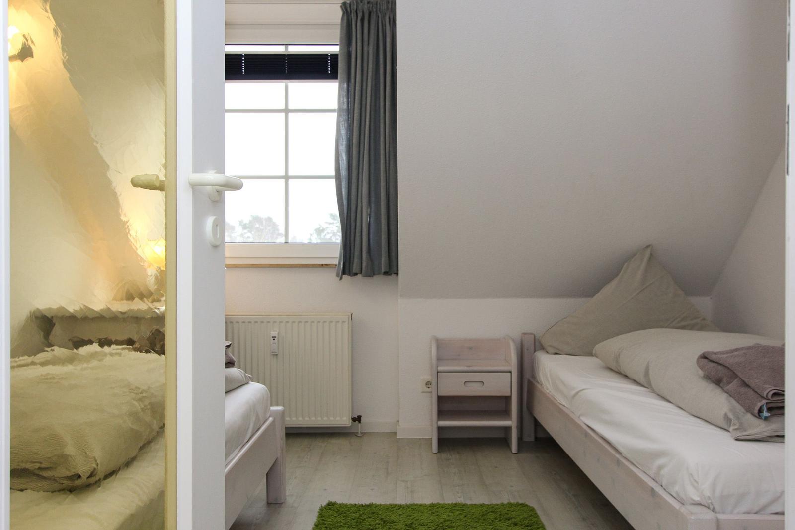 Schlafzimmer mit Dachschräge, Bett, Nachttisch und Fenster mit Vorhang.