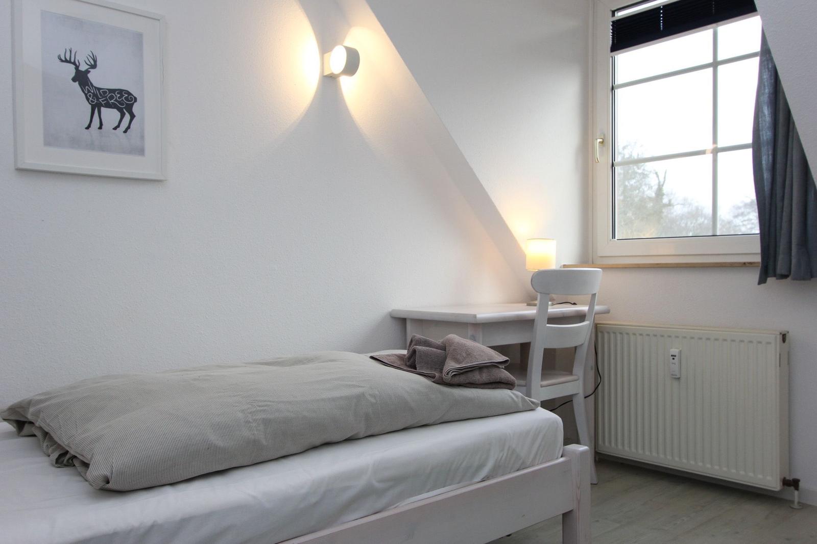 Ein Schlafzimmer mit Bett, Schreibtisch und Fenster. An der Wand hängt ein Bild mit einem Hirsch.