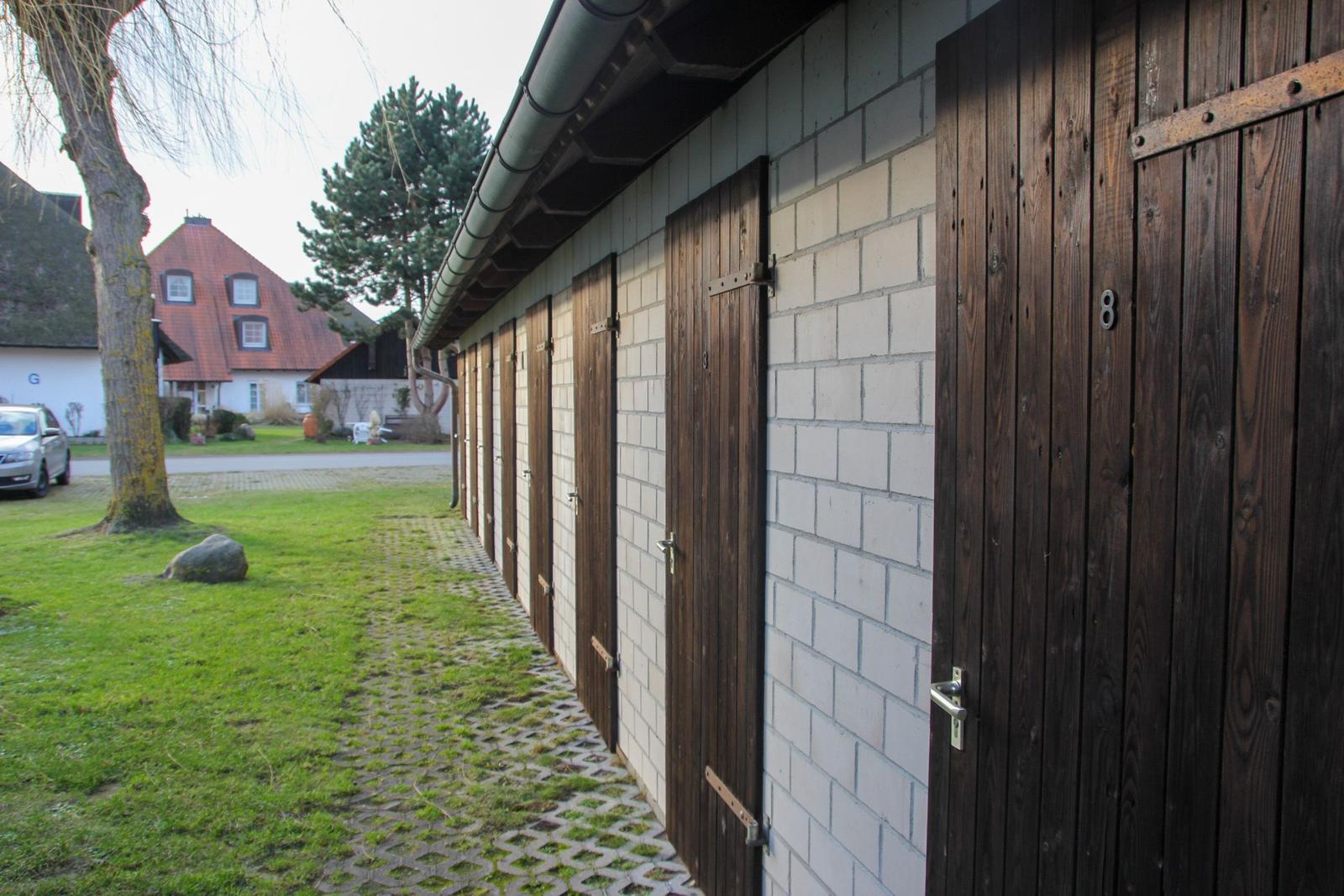 Reihe von Holztüren an einer weißen Ziegelwand mit gepflastertem Weg und Gras.