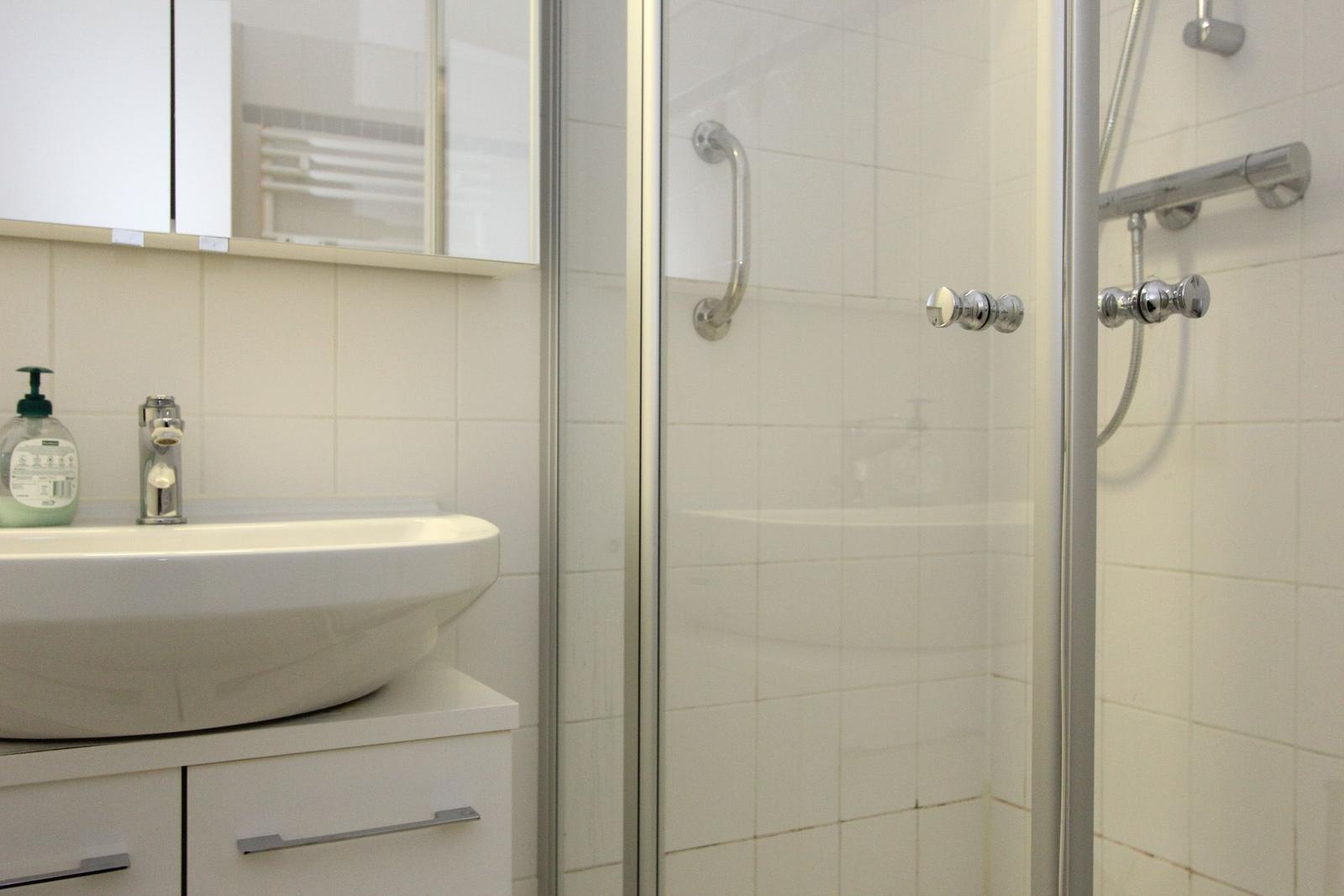 Badezimmer mit Dusche und Waschbecken. Weiße Fliesen und moderne Armaturen.