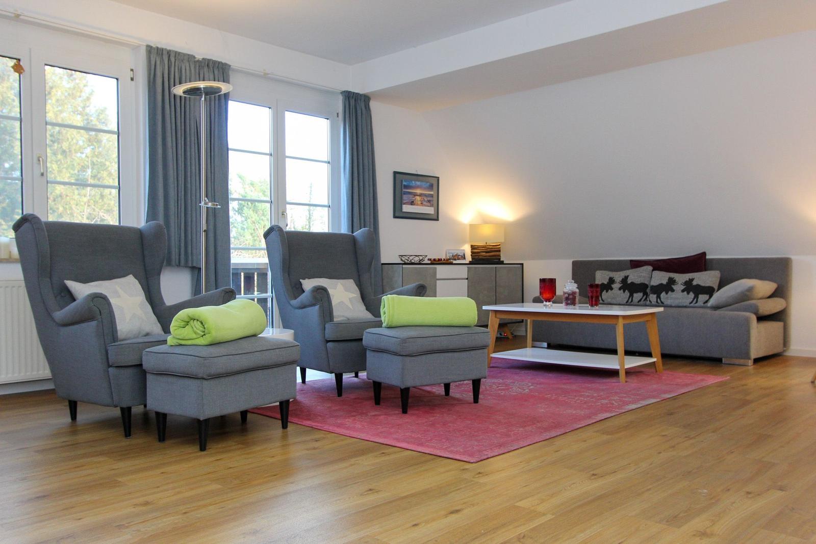Wohnzimmer mit grauen Sesseln, Sofa und Holzboden. Rote Teppich und Fenster mit Blick.