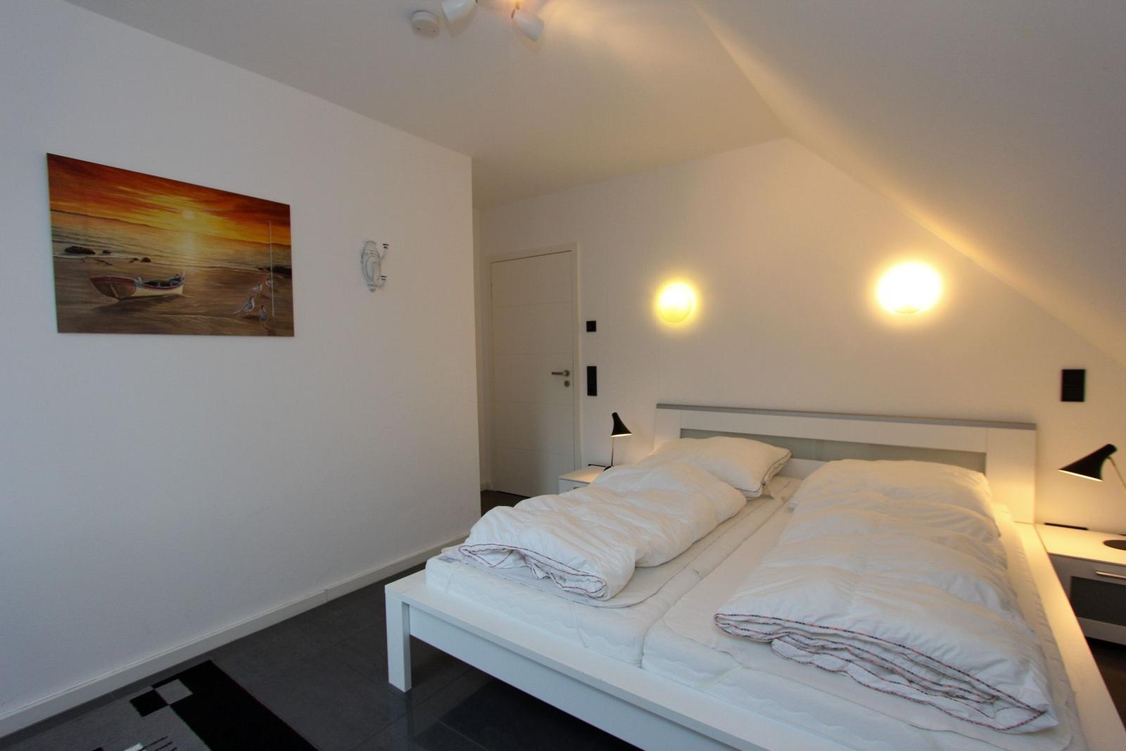 Schlafzimmer mit Doppelbett, Wandbild und Stehlampe.