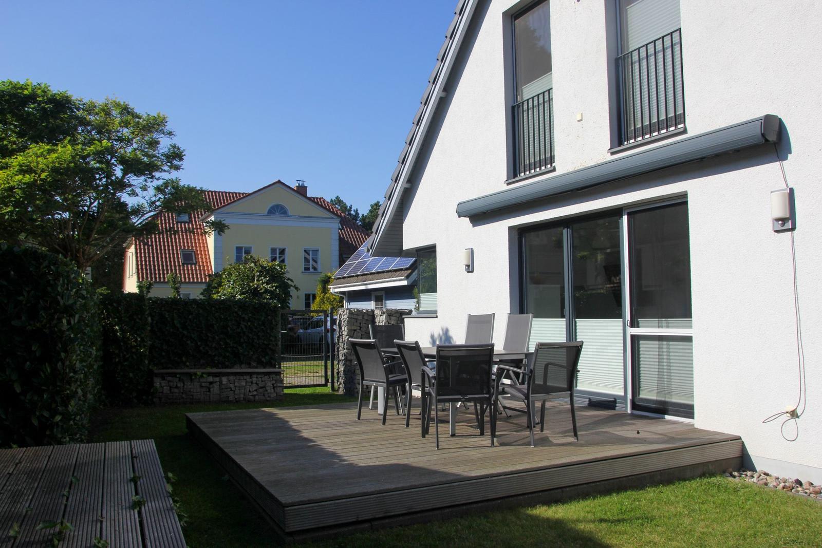 Terrasse mit Sitzgruppe vor modernem Haus mit Garten und Nachbarhaus im Hintergrund.